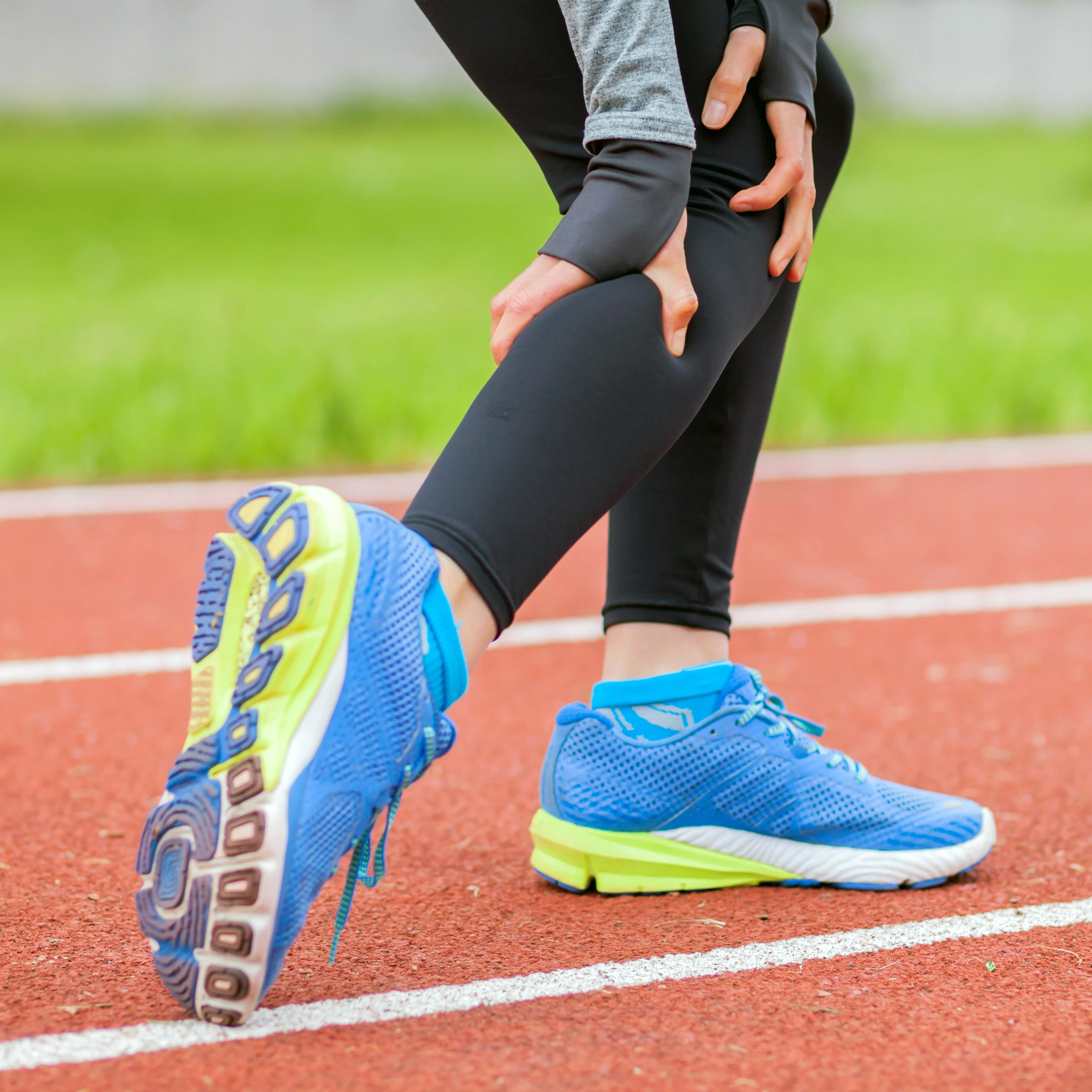 A track runner is holding their sore leg in discomfort. 