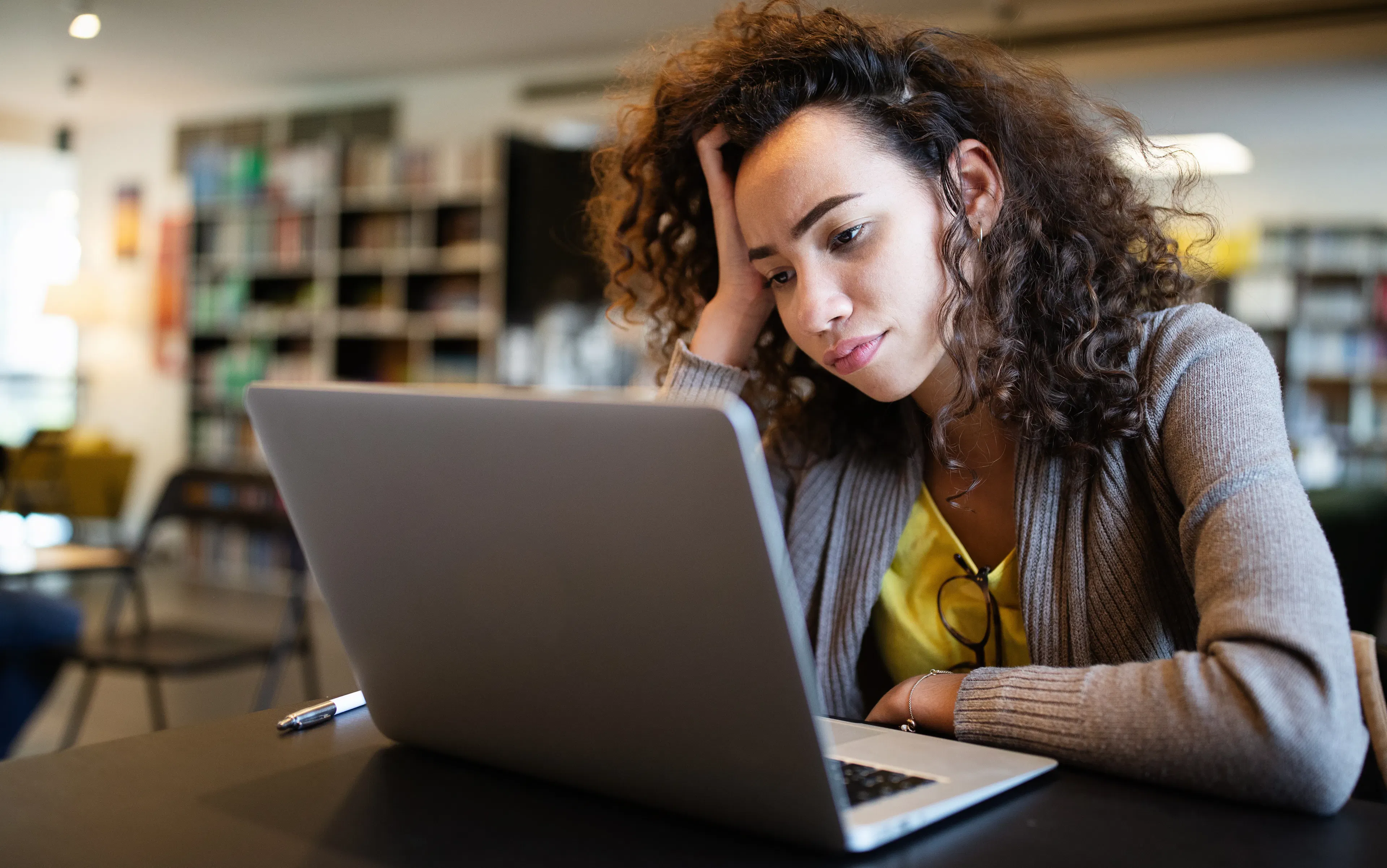 An adult woman is struggling to focus with her laptop in front of her.