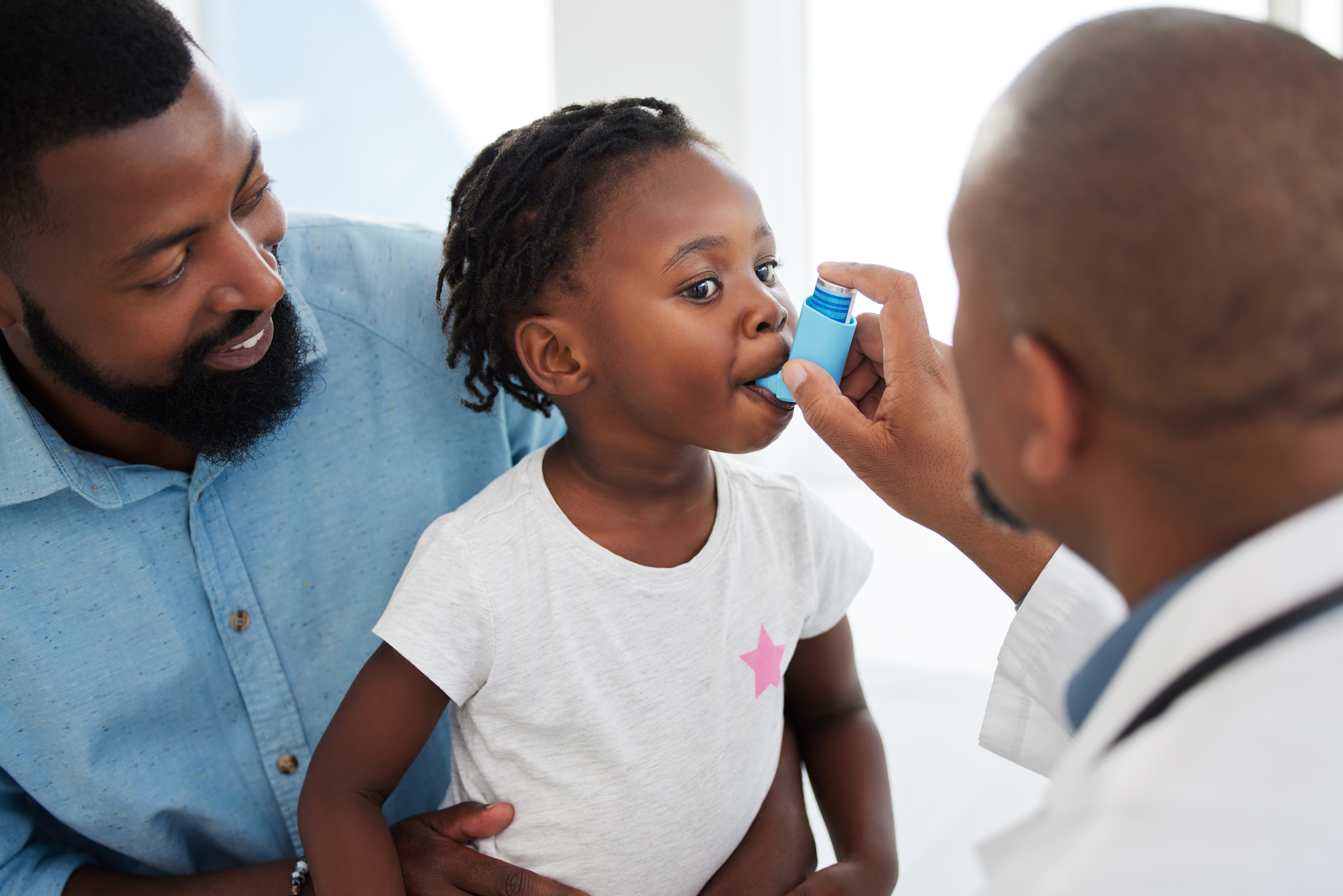 A young girl with asthma is seeing the doctor, who is helping her with an inhaler. 