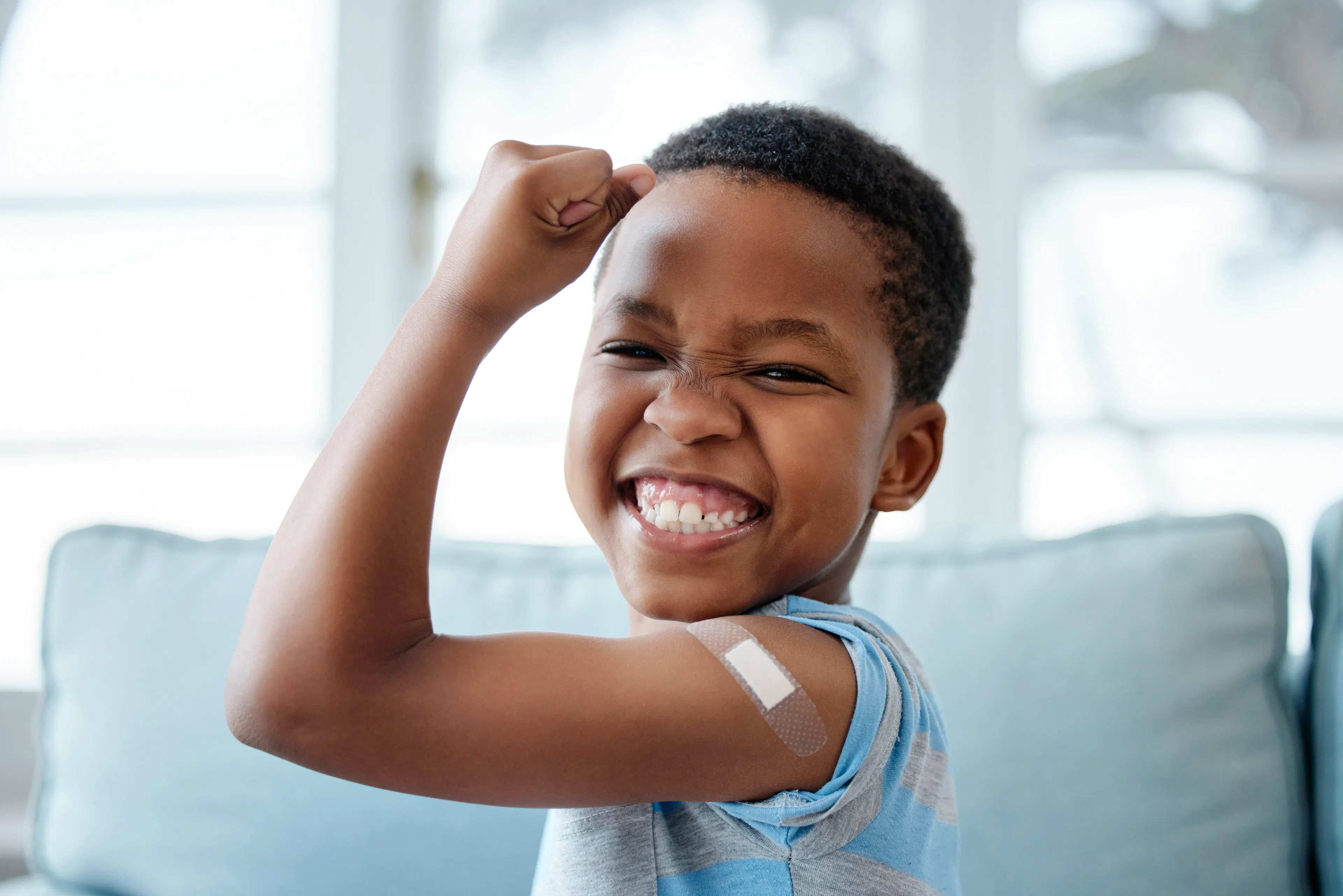 A child patient is flexing his arm with a band-aid while smiling after a health checkup.