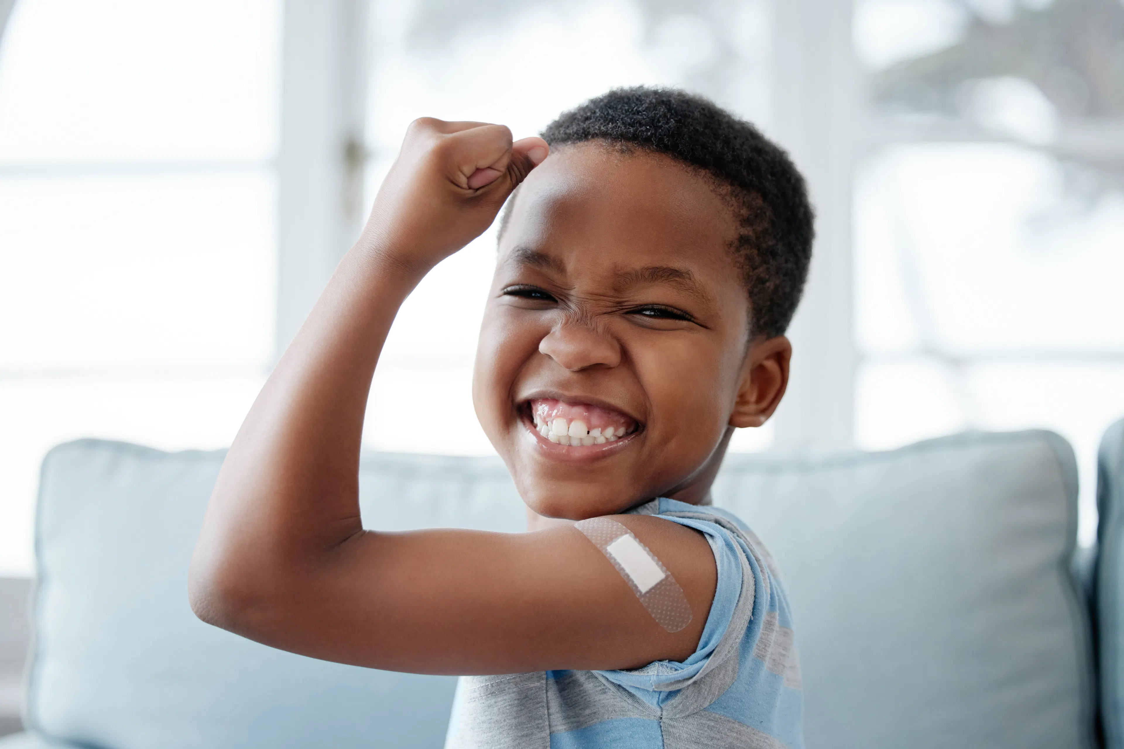 A child patient is flexing his arm with a band-aid while smiling after a health checkup.