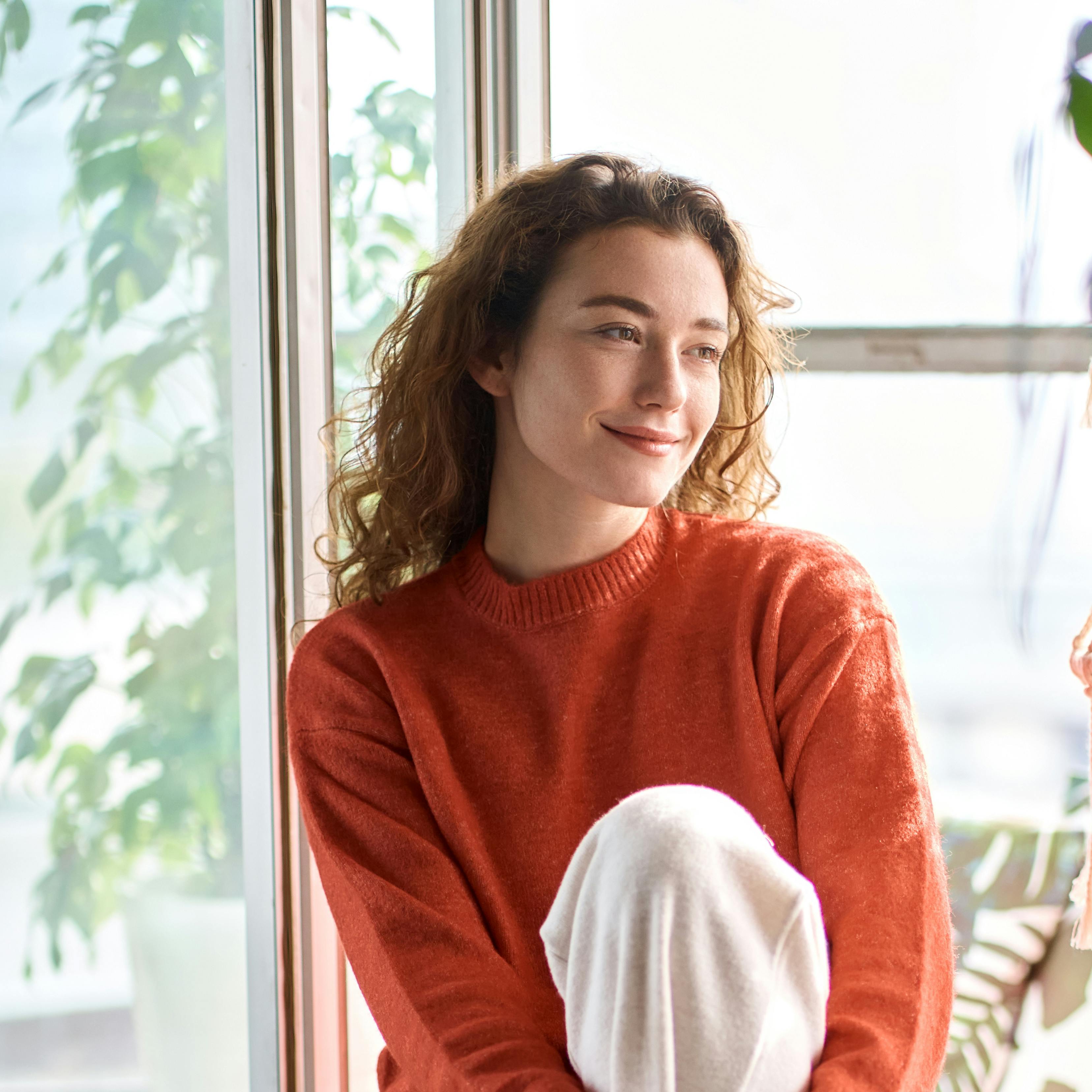 A woman is staring out her window with a content expression, seemingly at peace.