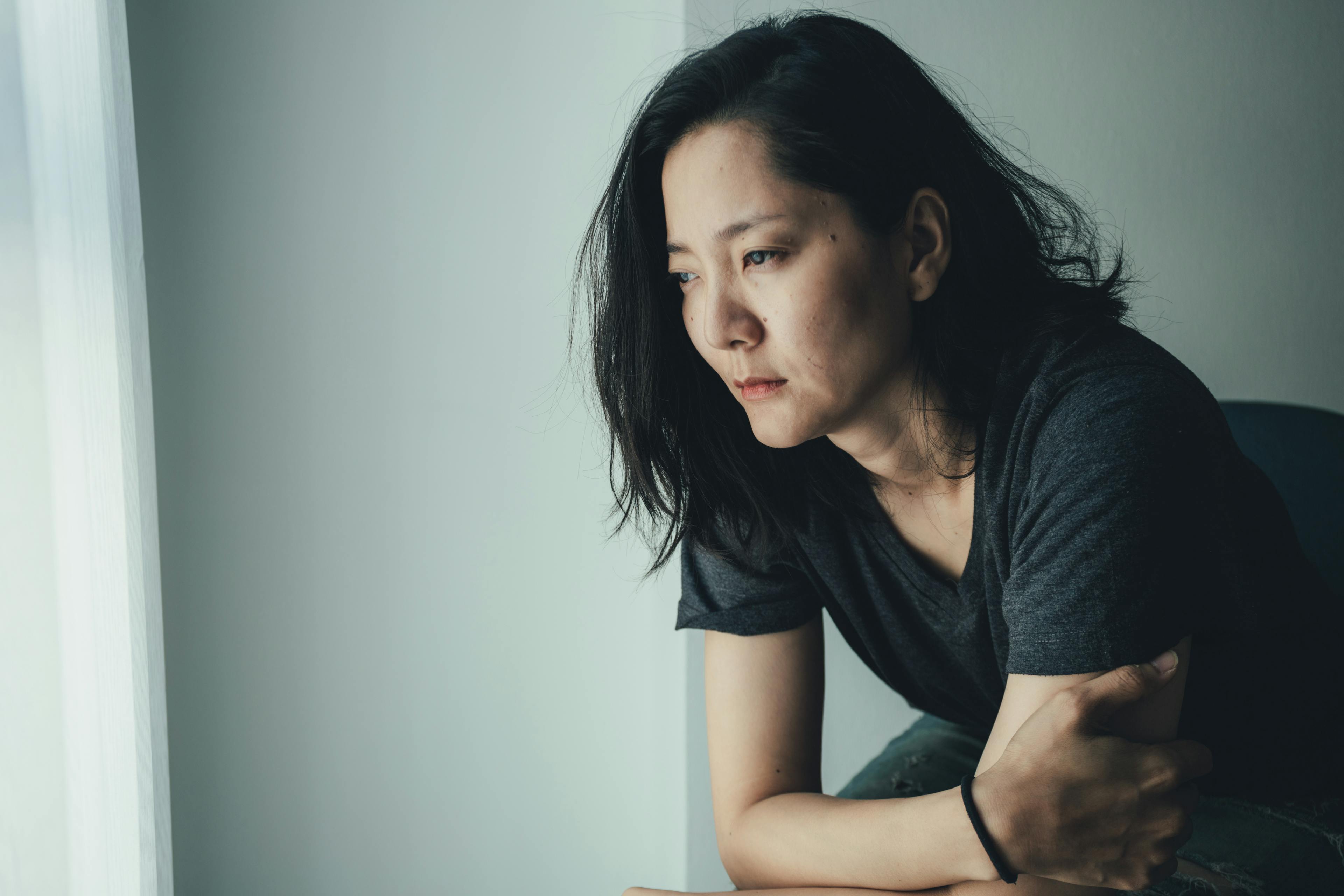 Depressed woman looking outside thoughtfully, showing signs of emotional distress and sadness.