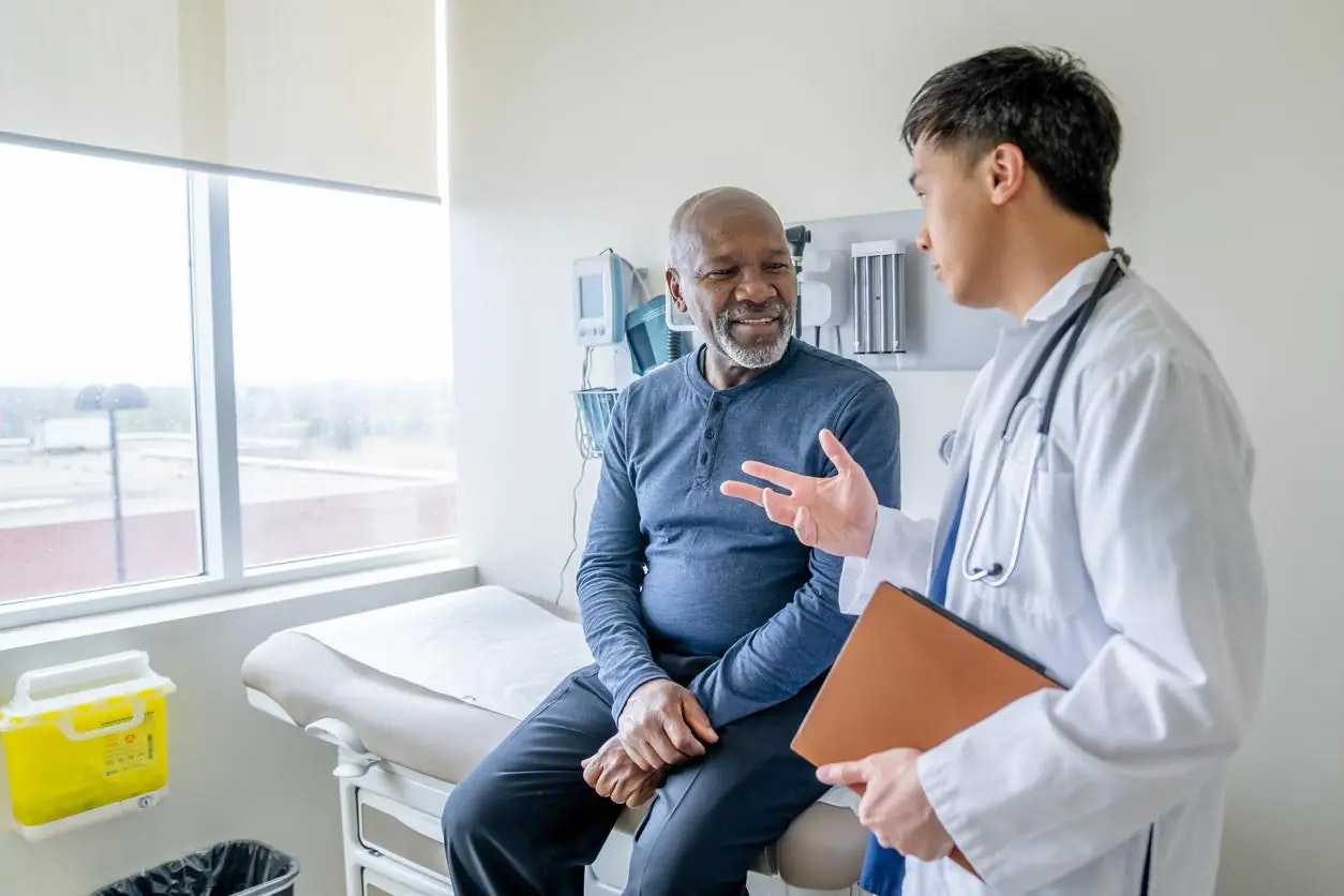 An image of a patient sitting in a doctor's office, speaking with a healthcare provider.