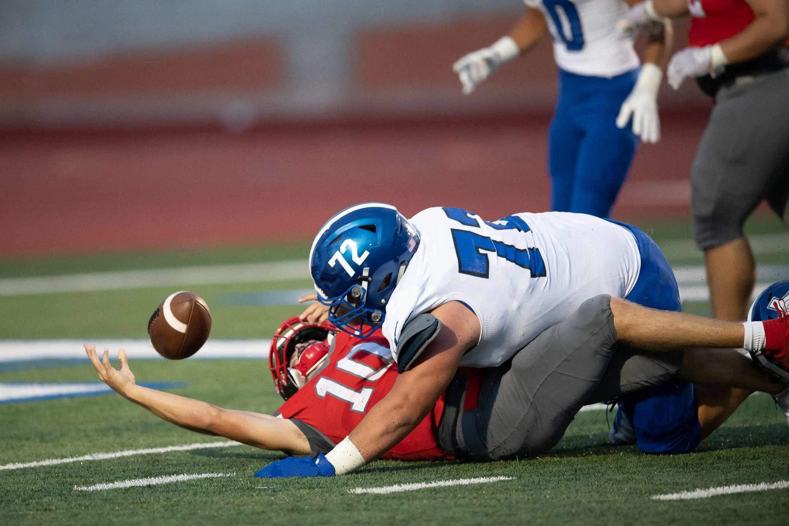 An intense high school football game , showing players in action. The scene emphasizes the risks of the 'no pain, no gain' mindset in youth sports.