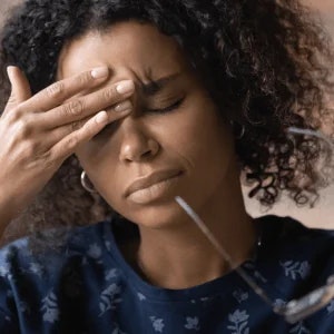 Woman with a pained expression, eyes closed, and fingers placed in the center of her forehead.