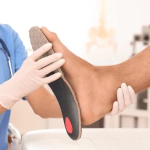 A podiatrist in scrubs holding an insole against the sole of a patient's foot.