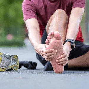 Male runner seated on pavement grasping his right foot.