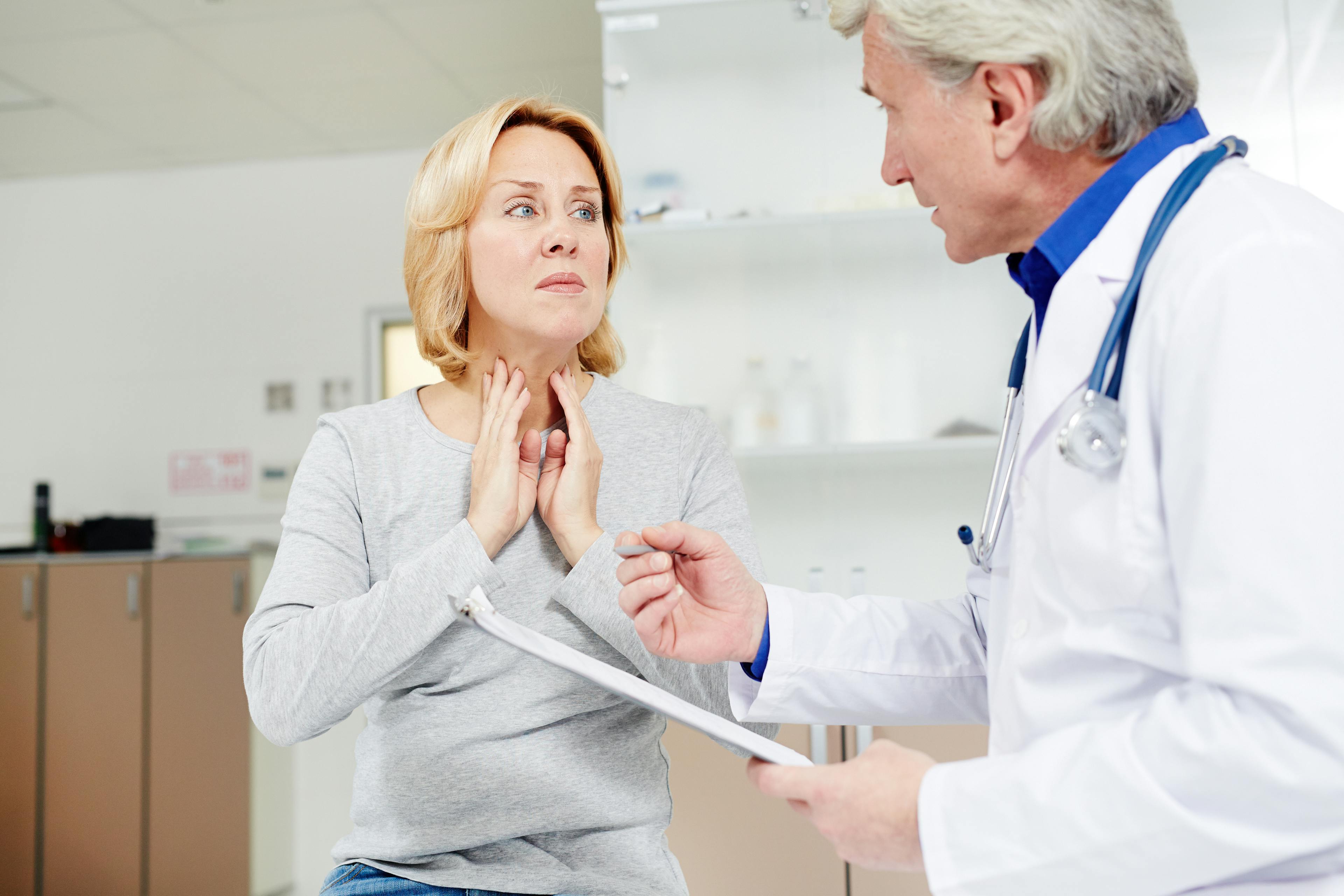 Physician attending to female patient with finger pressed to her throat.
