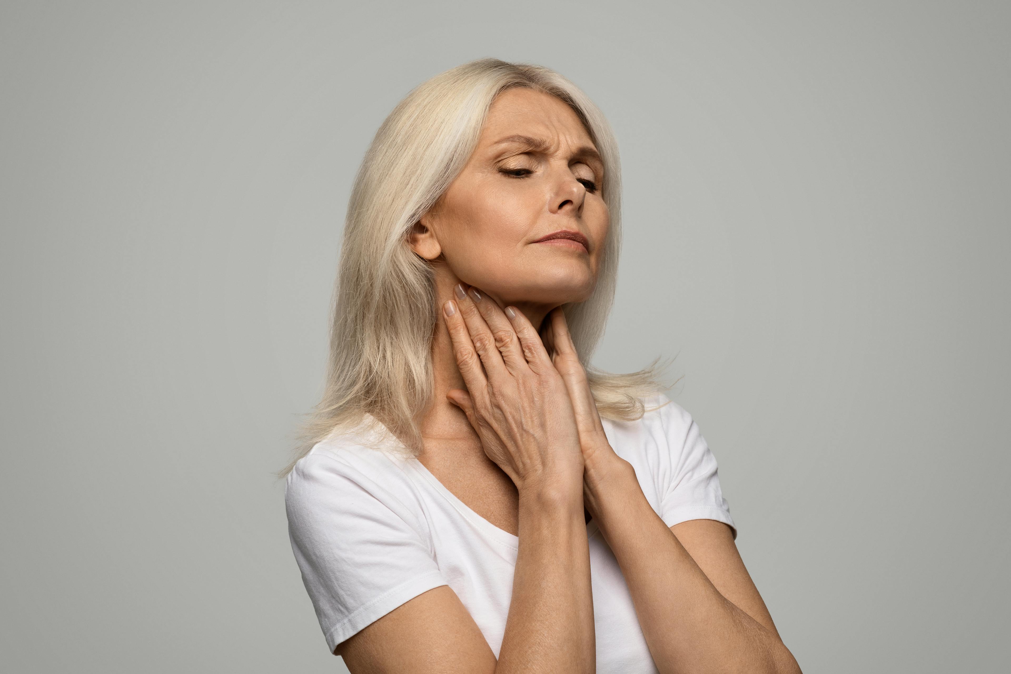 A woman with fingers placed on her throat in a gesture of discomfort and pain.