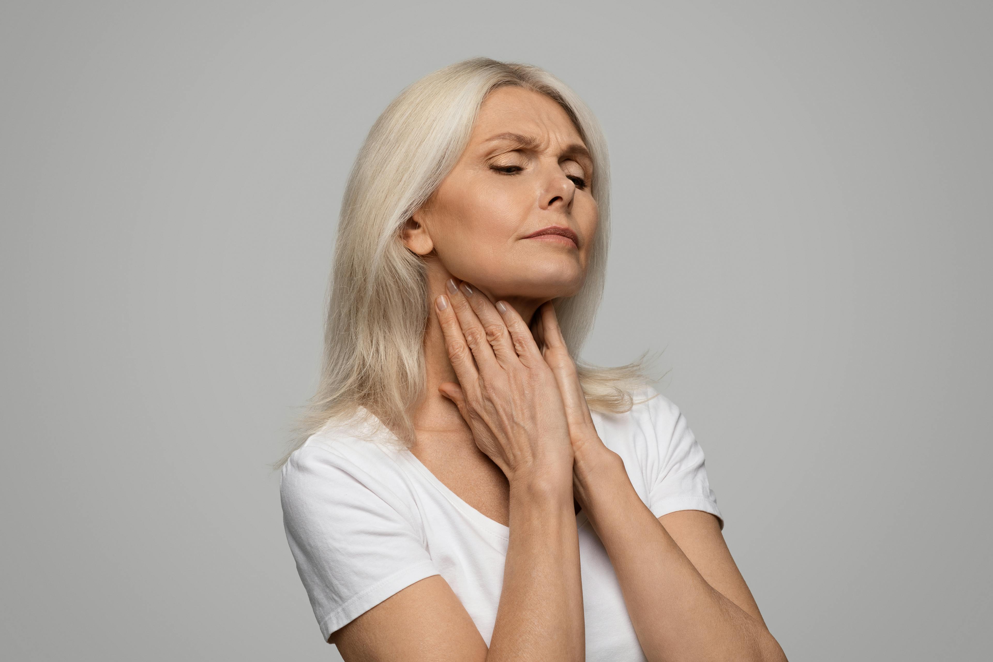 A woman with fingers placed on her throat in a gesture of discomfort and pain.