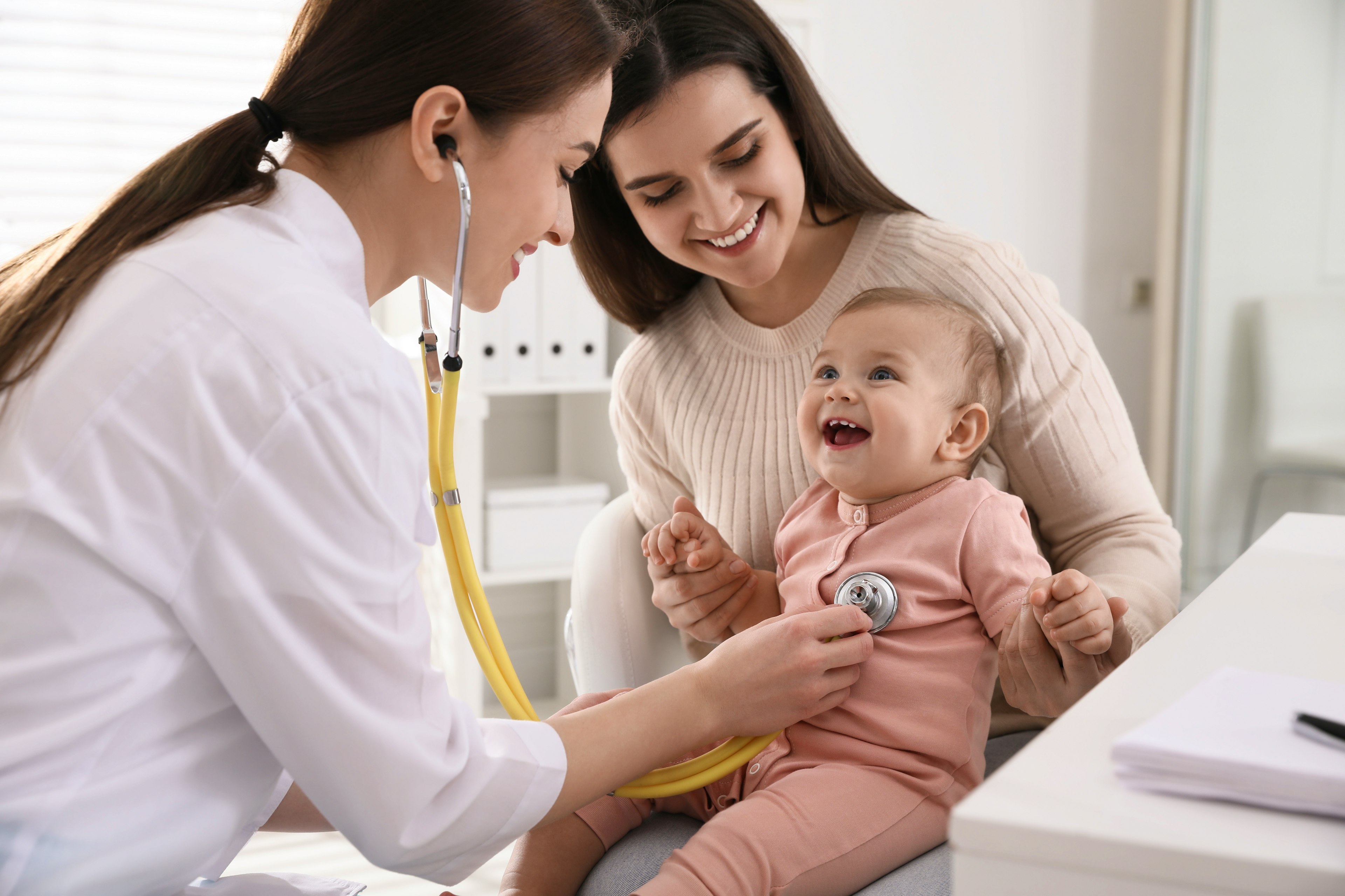 A female healthcare provider examines a child while she rests on mother's lap.