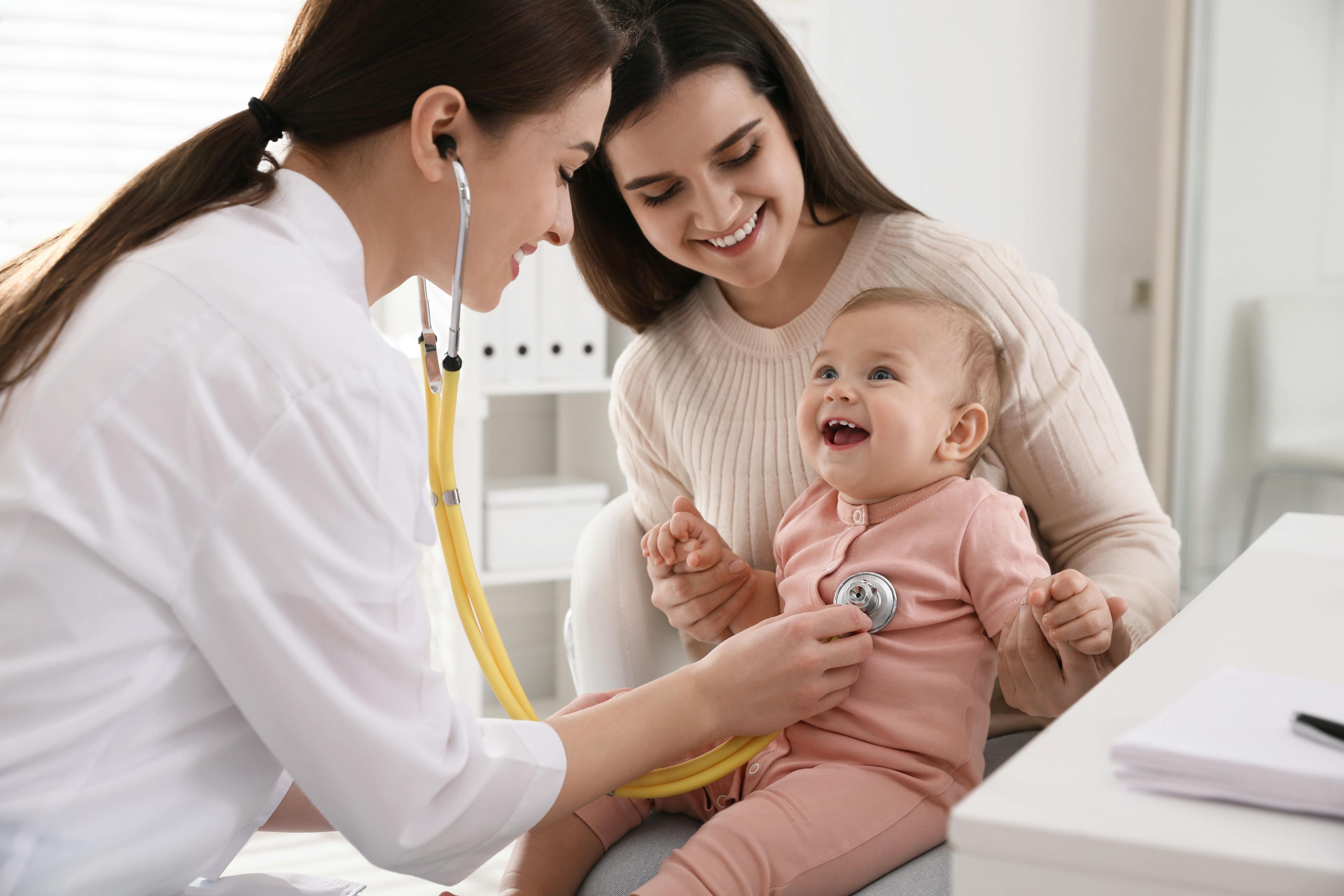 A female healthcare provider examines a child while she rests on her mother's lap.