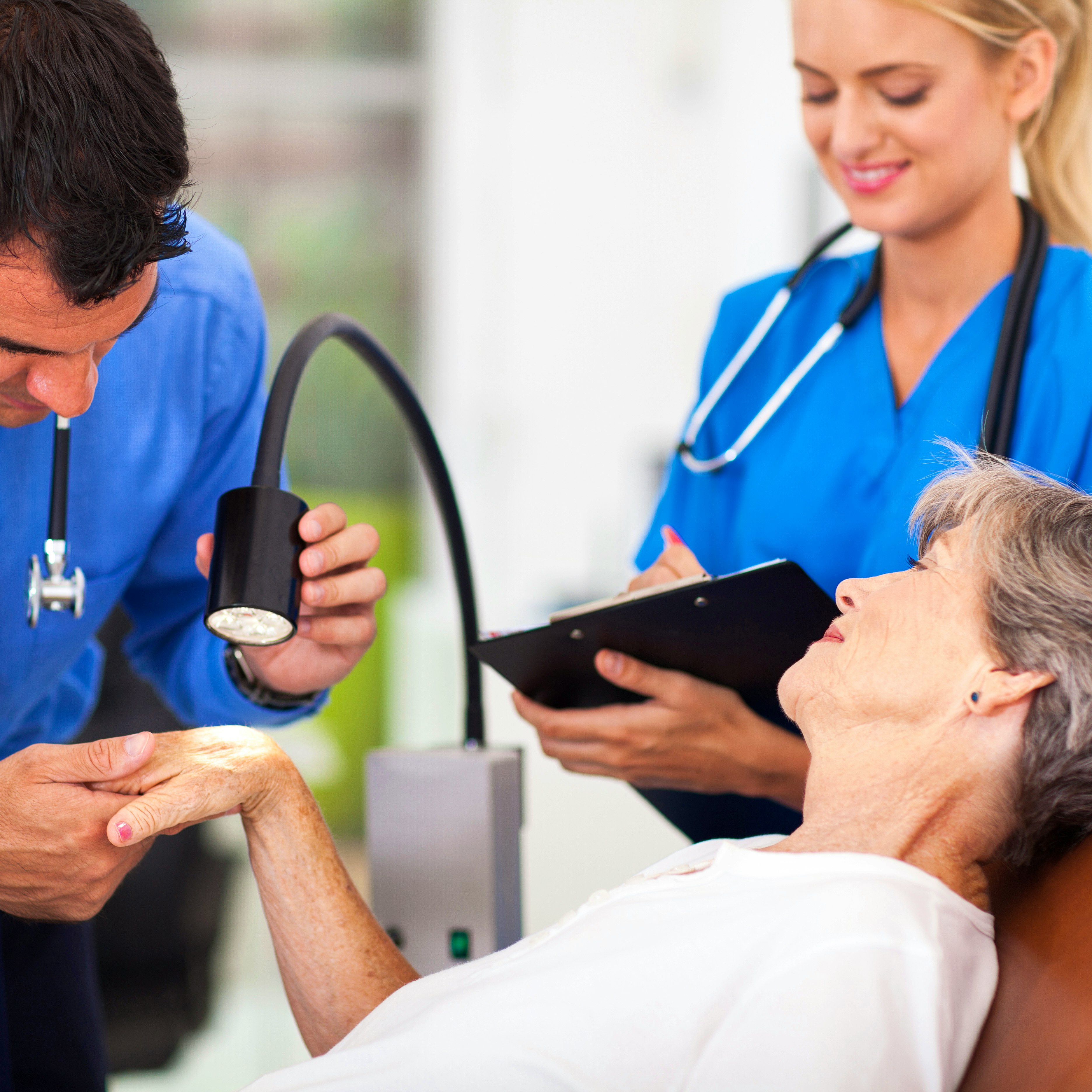 A doctor using a light instrument to examine skin on a patient's hand.