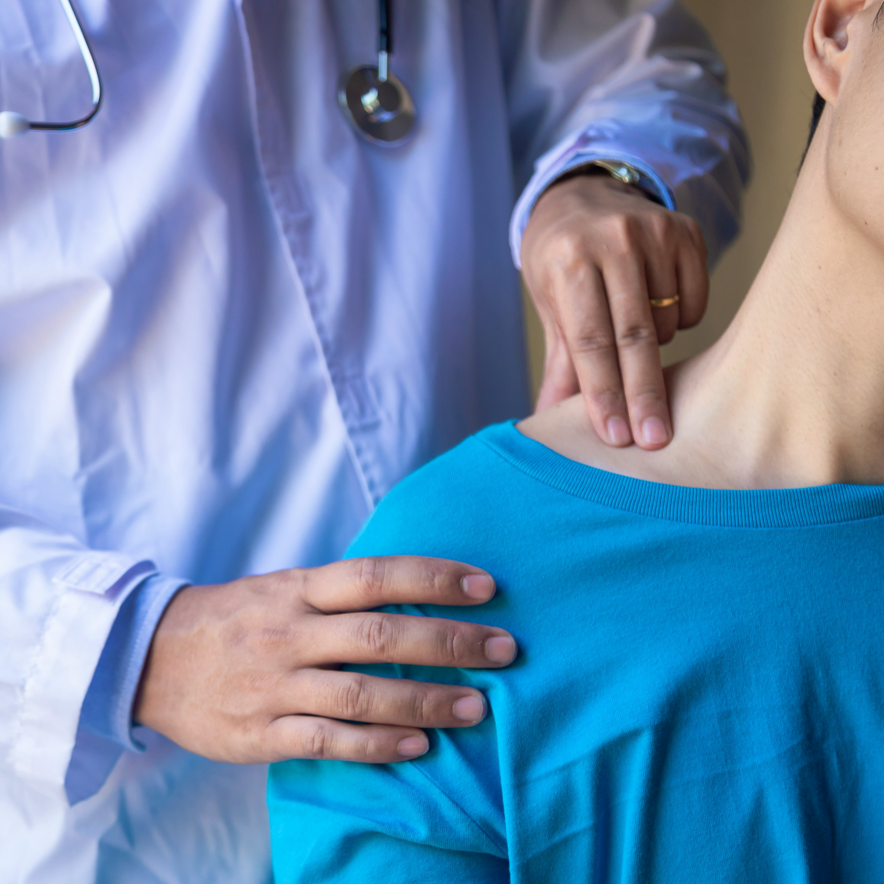 A physician conducing a physical examining a female patient's shoulder region.