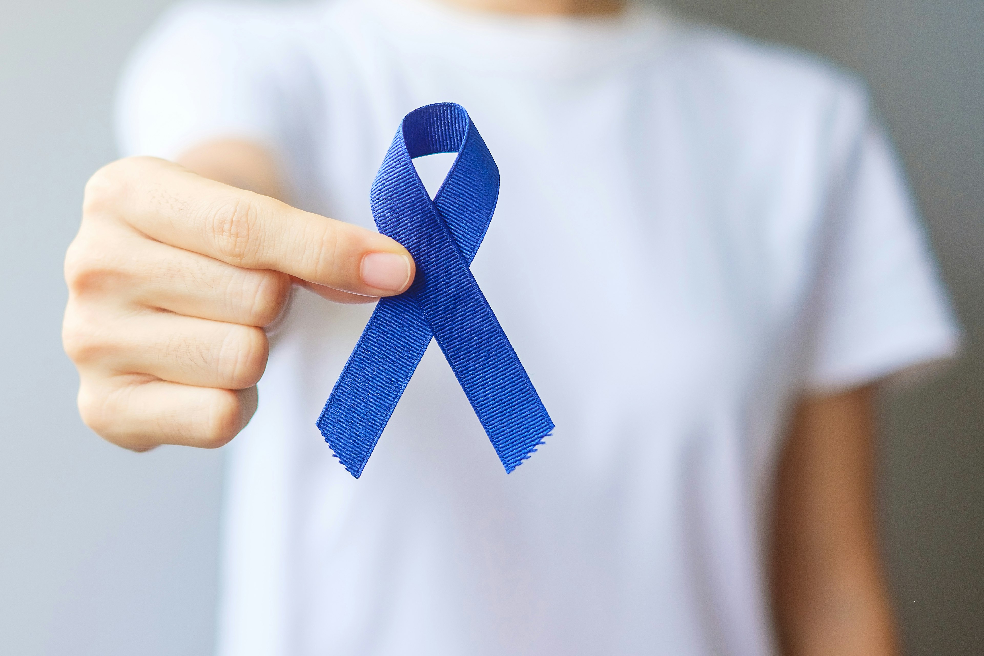Person holding a blue ribbon representing colorectal awareness.