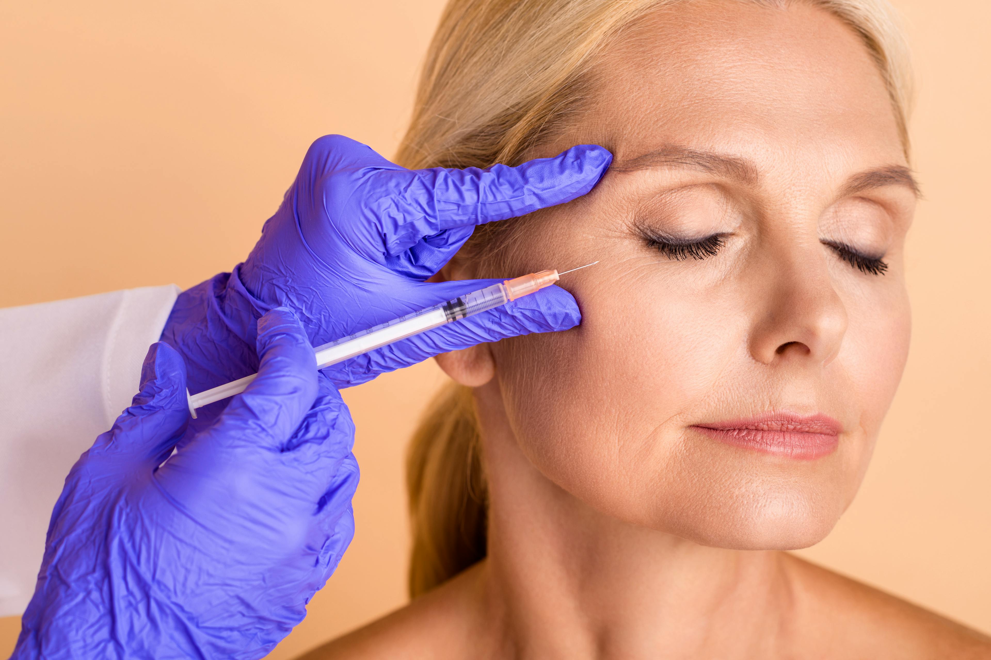 A middle-aged female patient receiving a dermal filler injection on her upper right cheek.