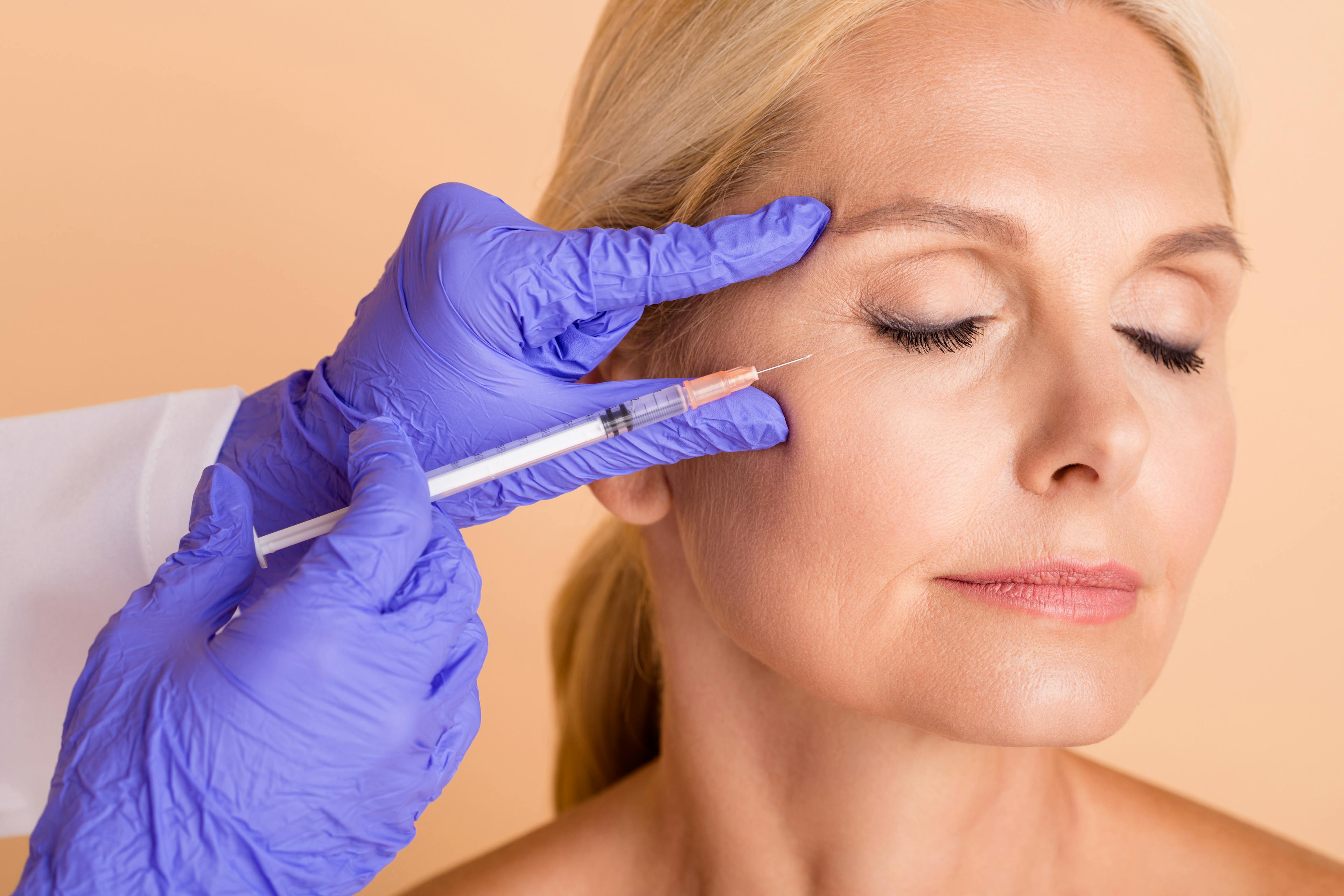 A middle-aged female patient receiving a dermal filler injection on her upper right cheek.