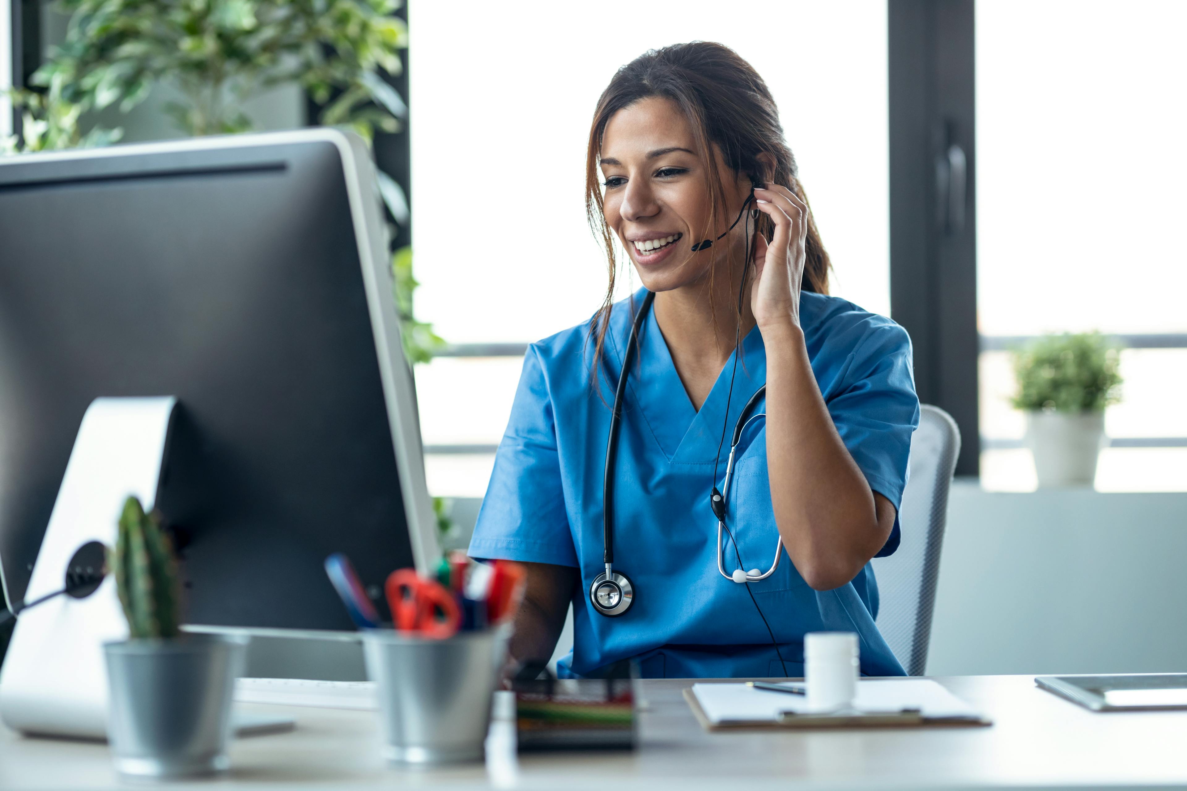 Picture of a medical worker with a headset sitting at a computer receiving a call from a patient.