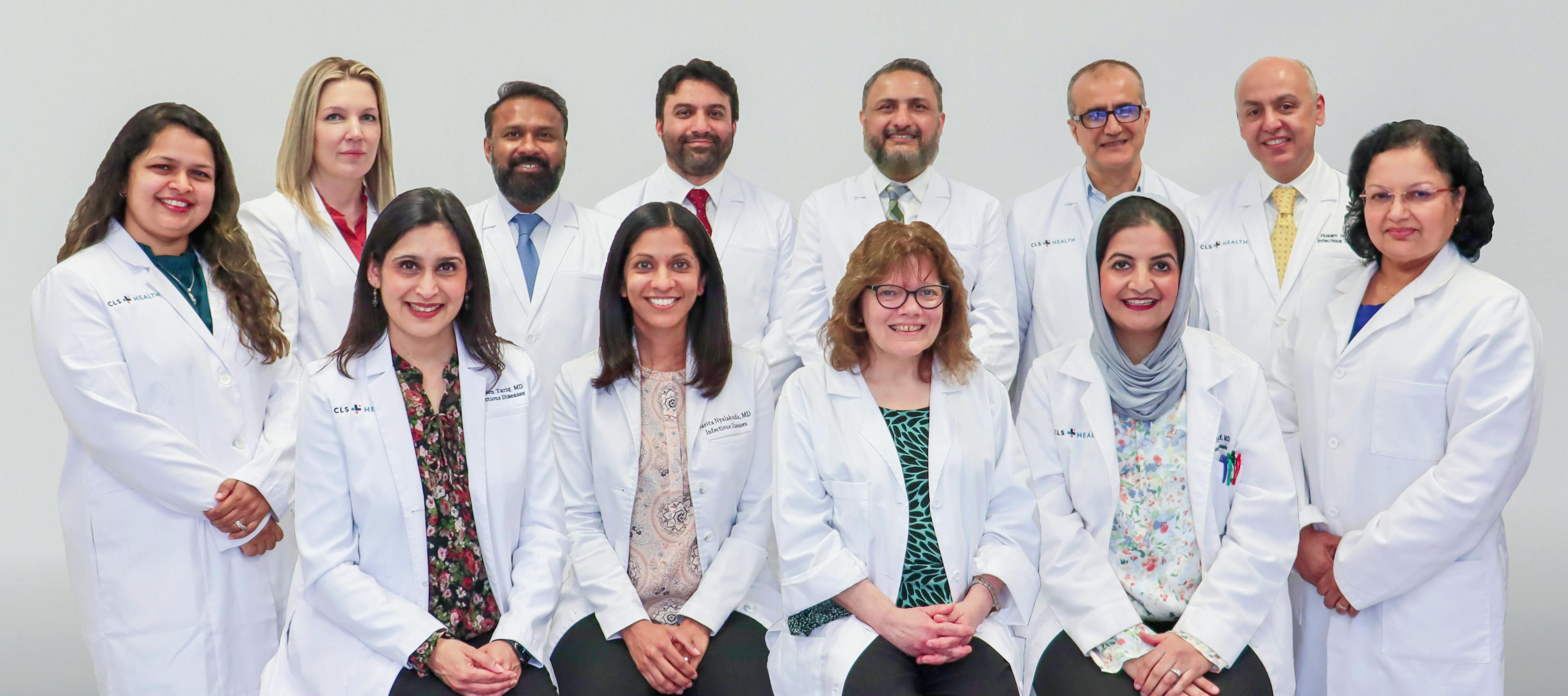 Group photo of CLS Health infectious disease doctors wearing white coats, standing together and smiling at the camera.