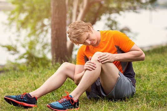 A man sitting in grass observing his knee due to arthritis pain.