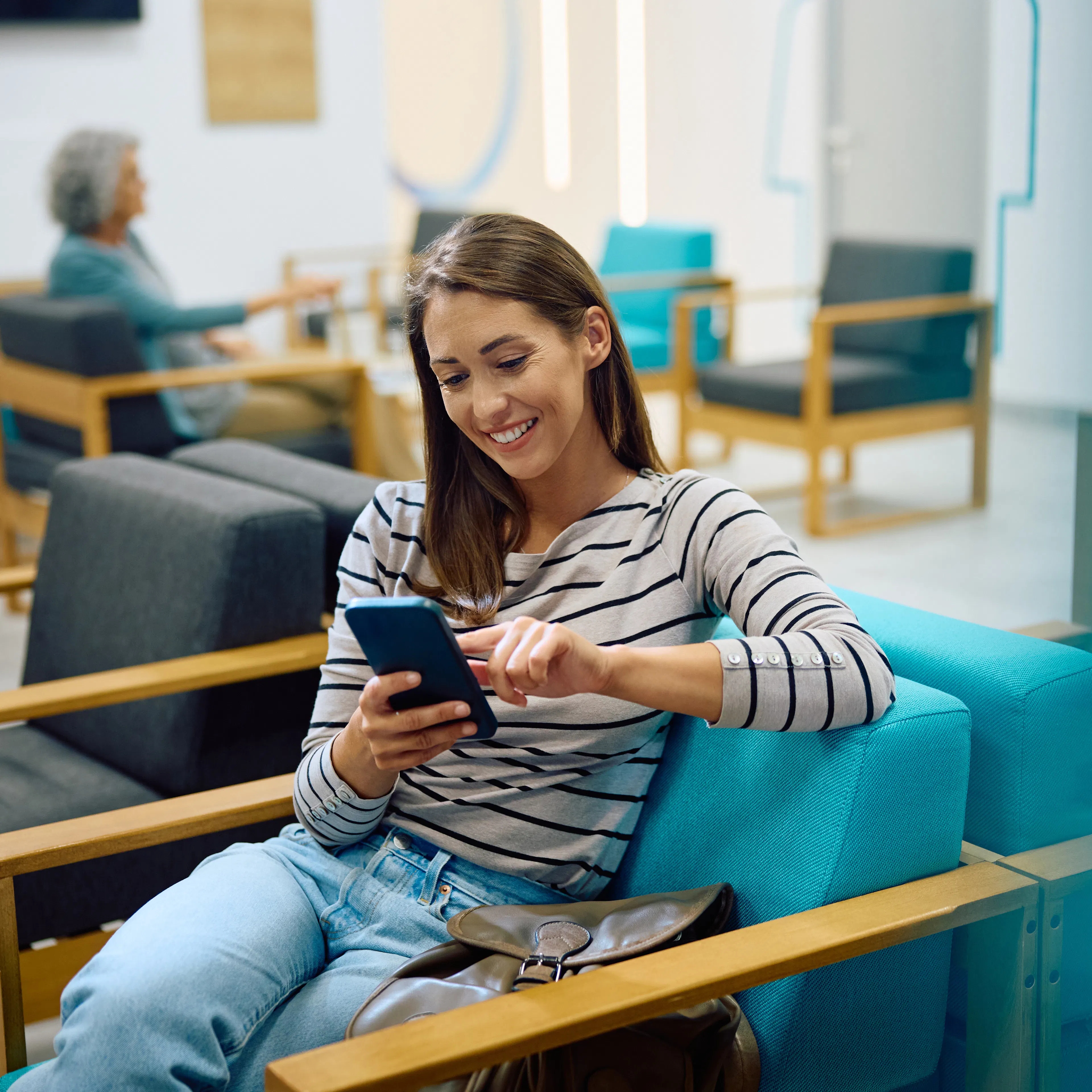 A female healthcare patient is sitting in a clinic lobby while using her phone. 