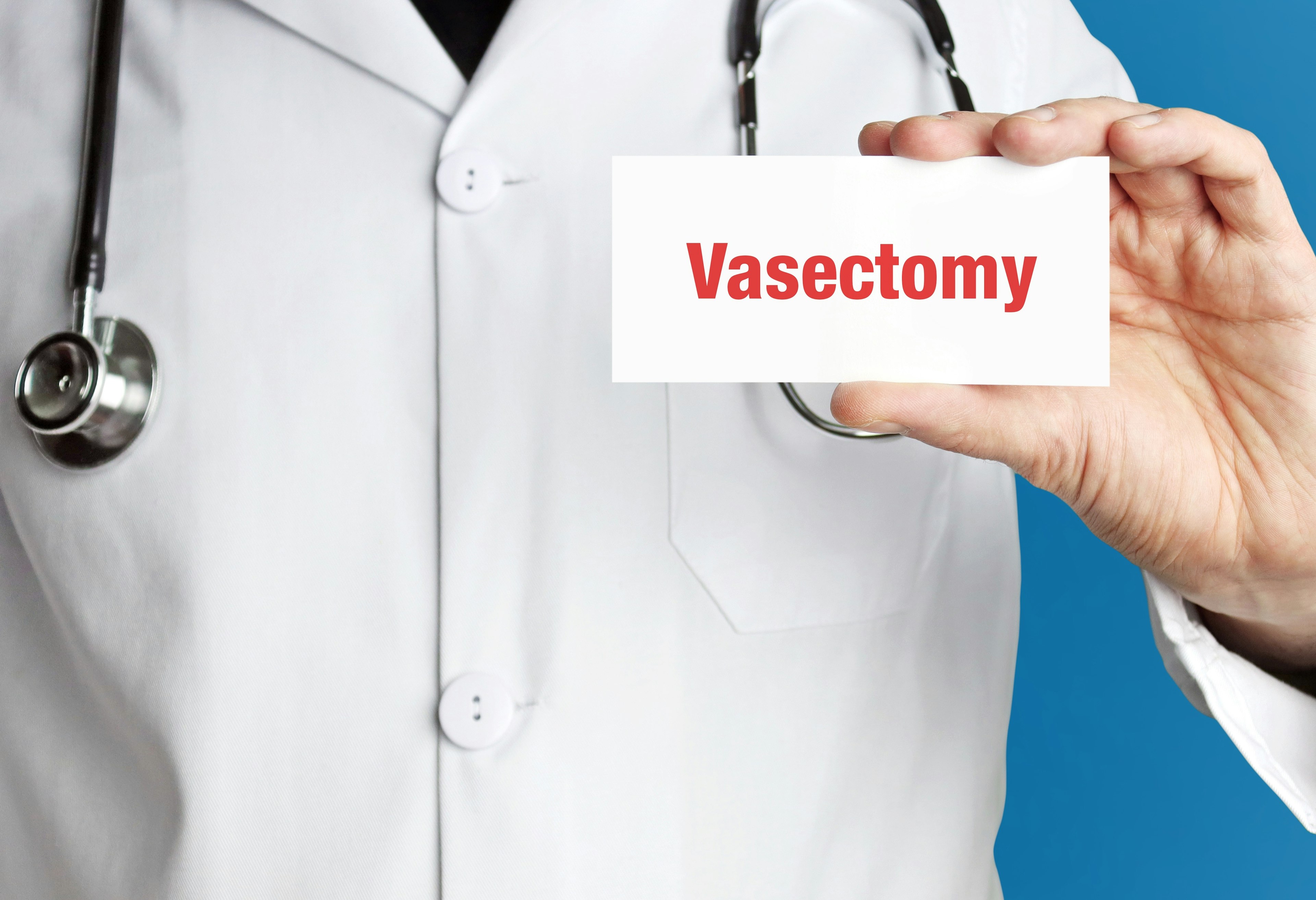 Doctor in white lab coat holds up business card. The term Vasectomy is in the sign.