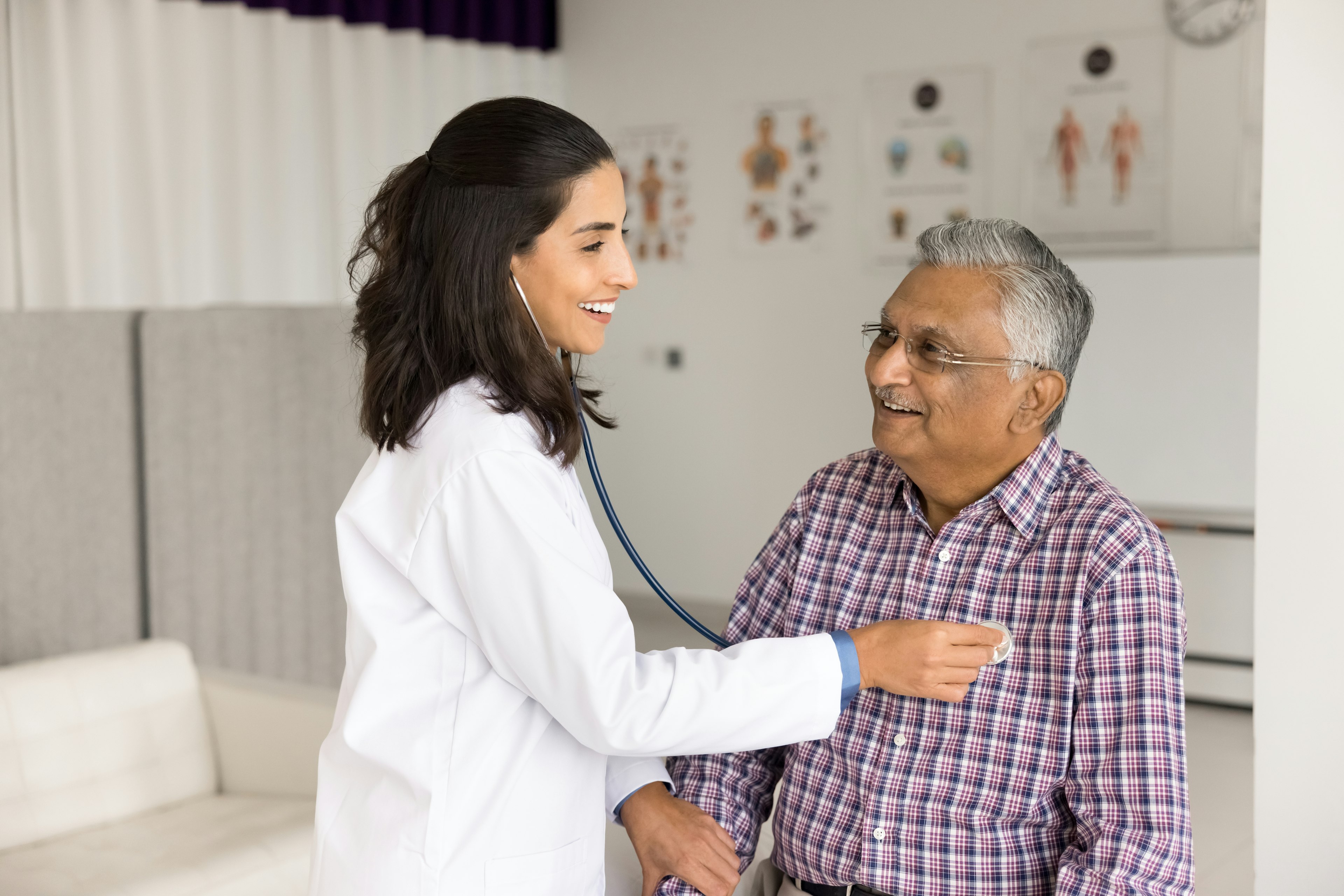 A doctor is using her stethoscope to check her male patient's heartbeat. 