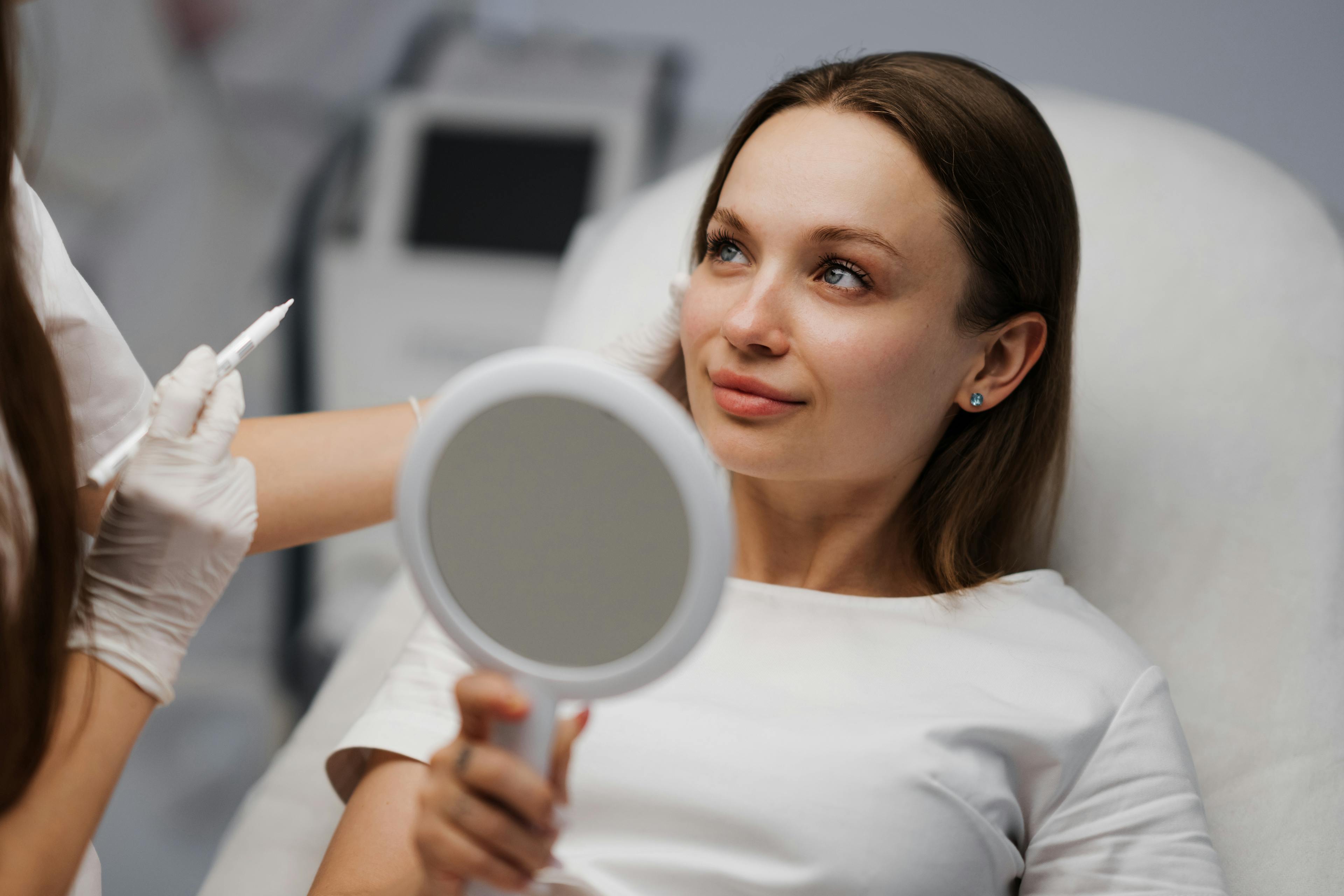 A cosmetic patient is looking at her provider happily while holding a mirror.