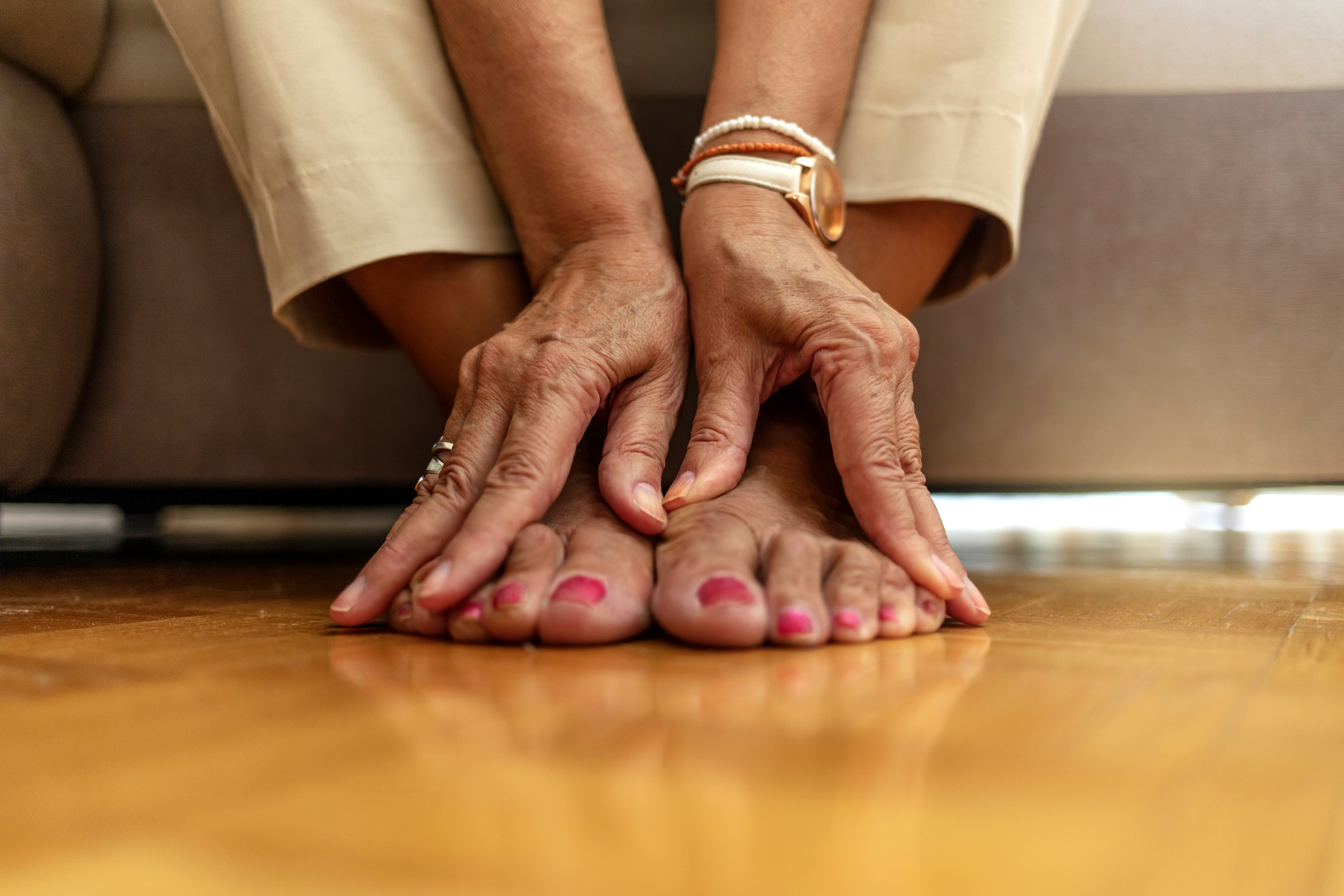 Close-up of an older adult sitting on the floor, gently touching their bare feet with both hands.