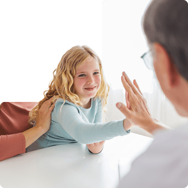 Smiling young girl giving a high-five to an older adult wearing glasses, while a supportive adult hand rests on her back.