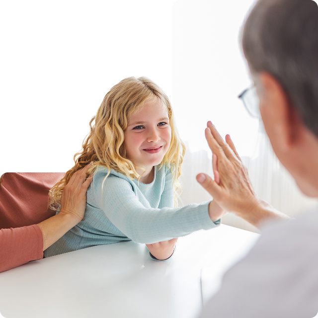 Smiling young girl giving a high-five to an older adult wearing glasses, while a supportive adult hand rests on her back.