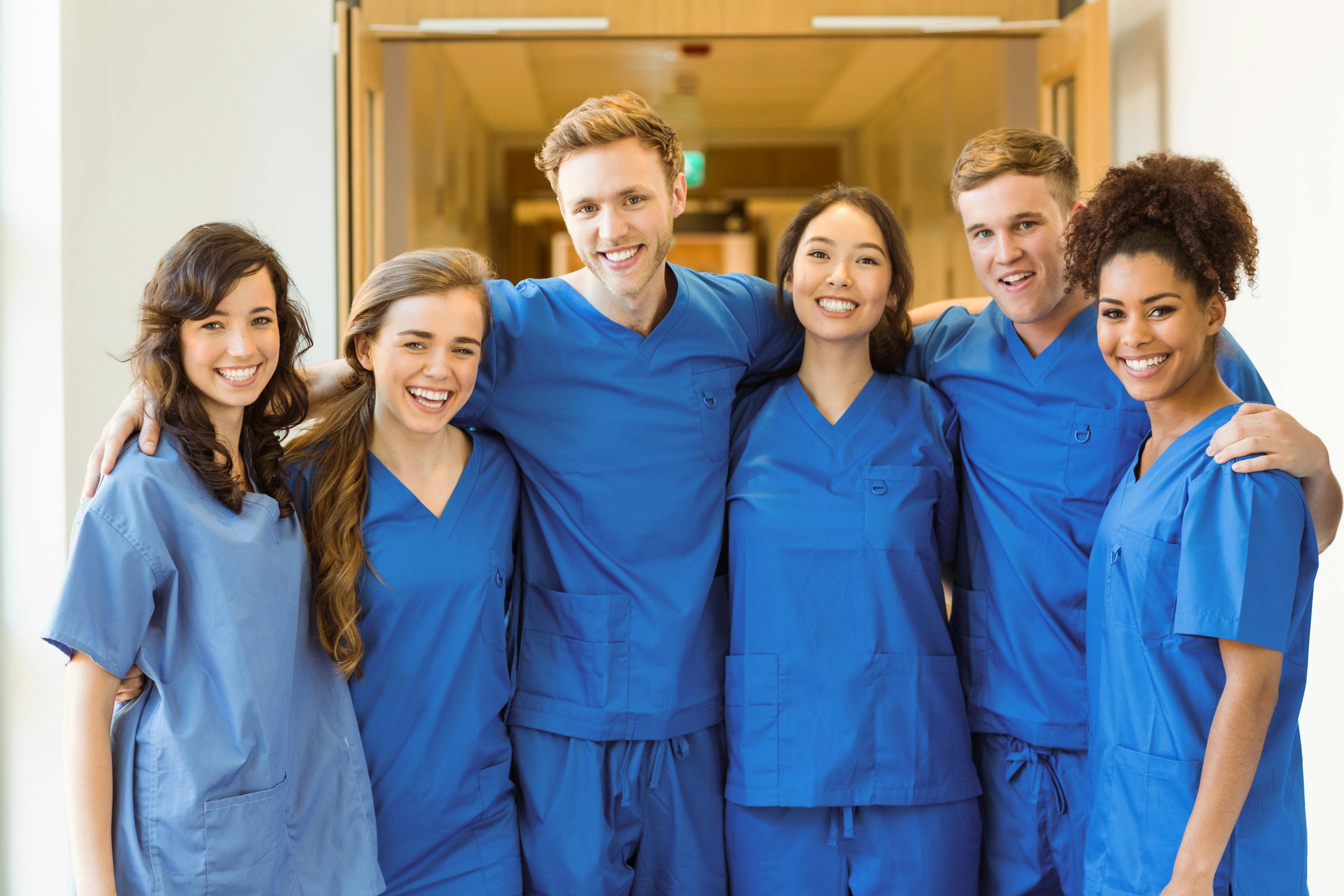 A group of medical students pictured with blue scrubs, posing together for a group photo, showcasing teamwork. 