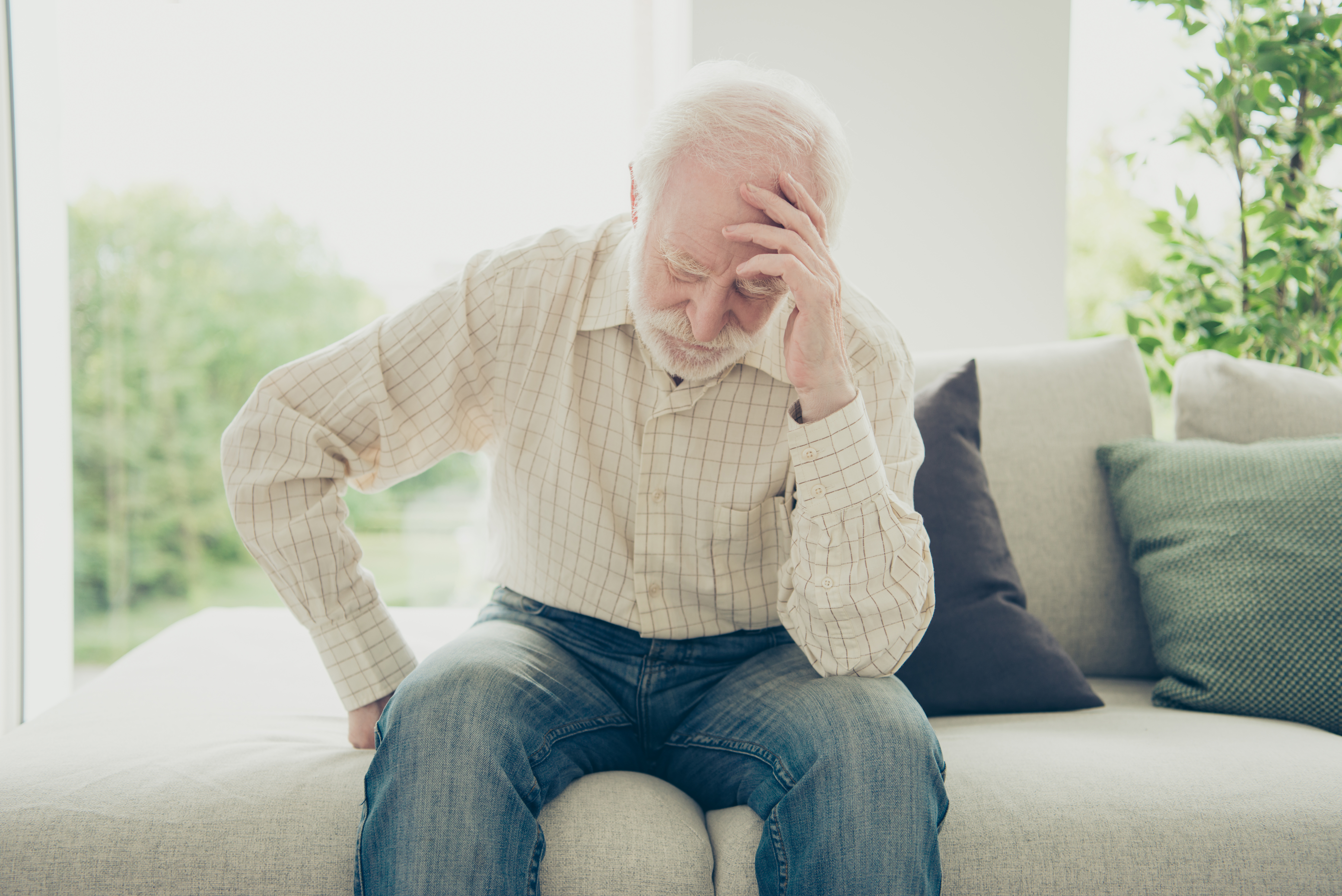An elderly man is holding his head in pain. 