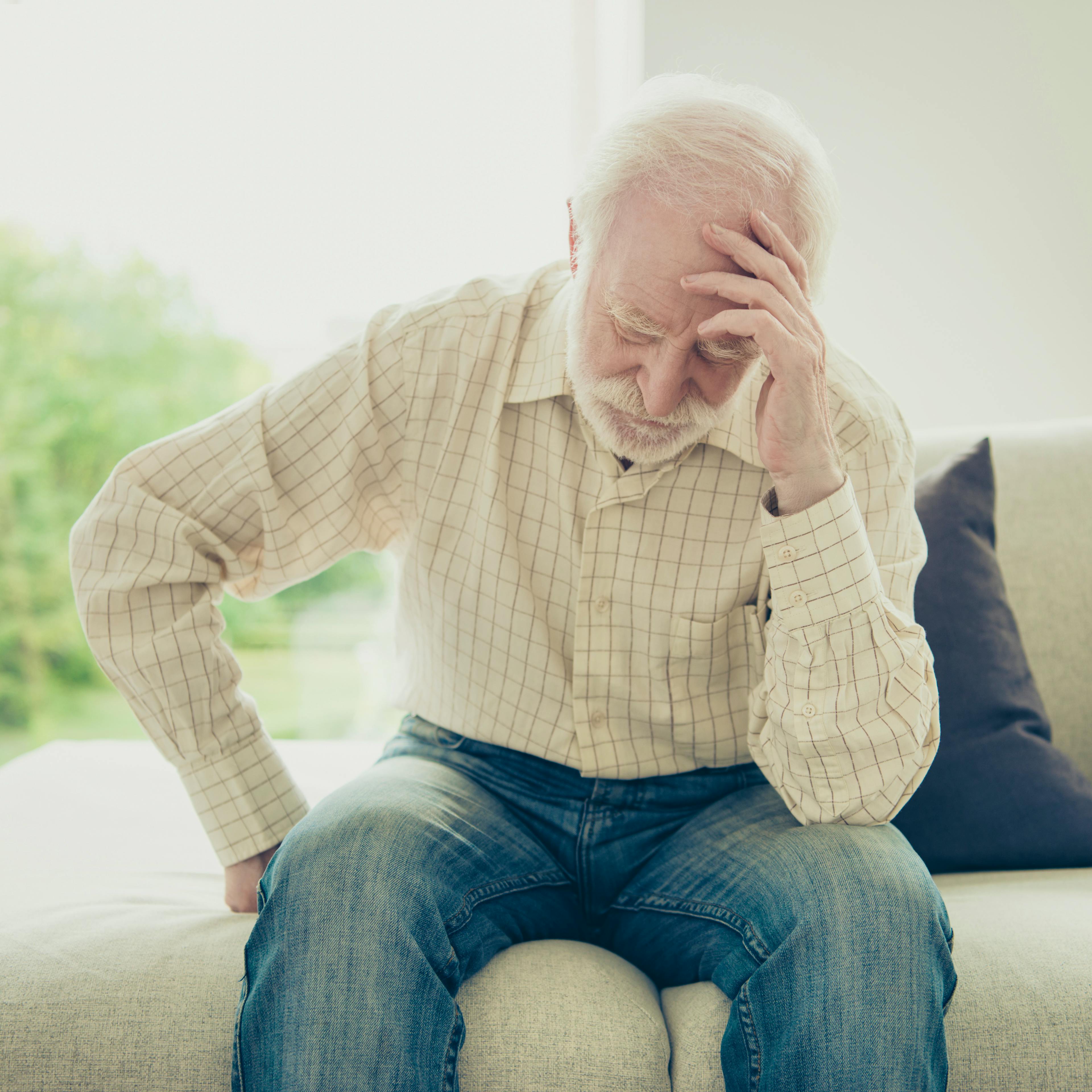An elderly man is holding his head in pain.