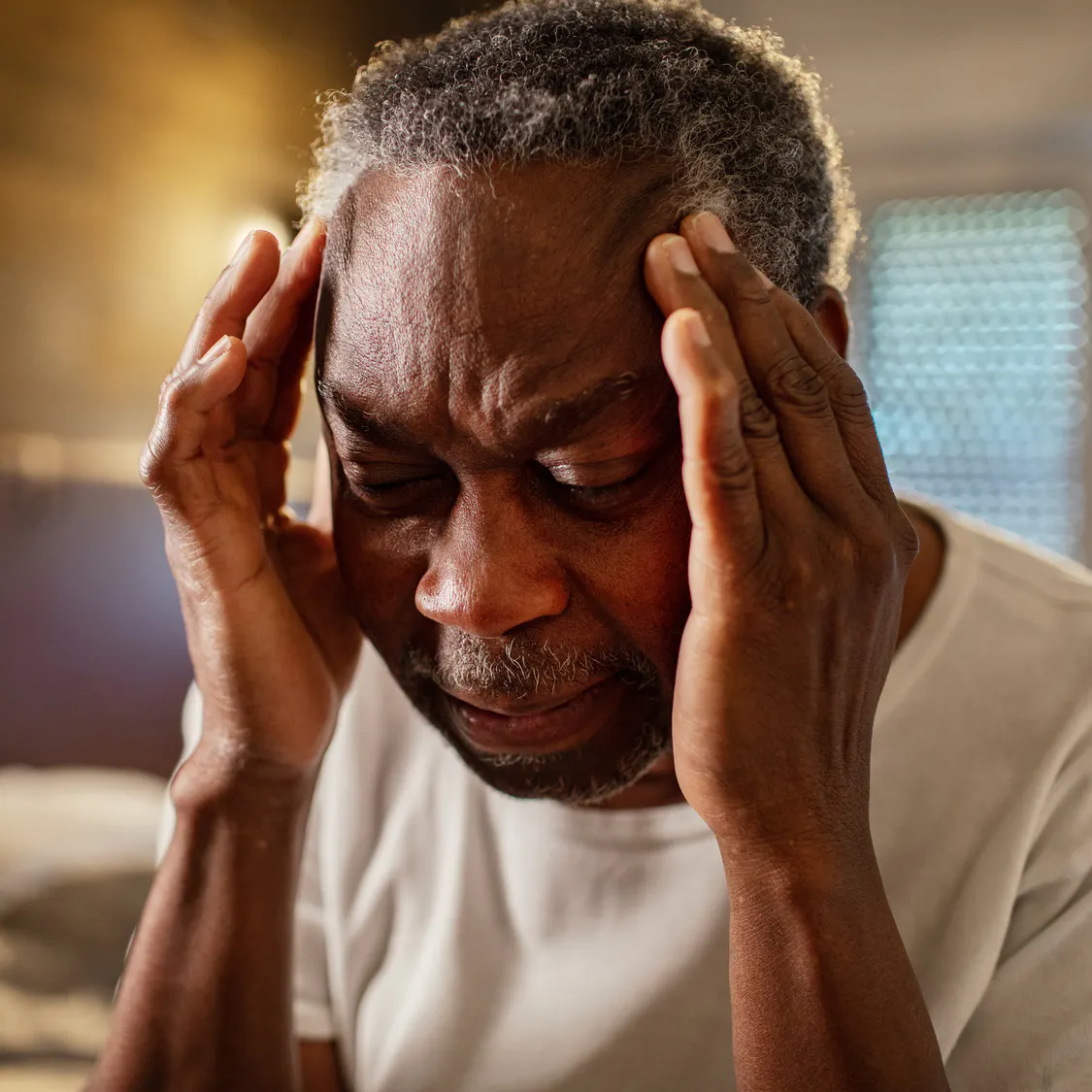 A man is holding his head in pain due to head pain, possibly due to stroke.