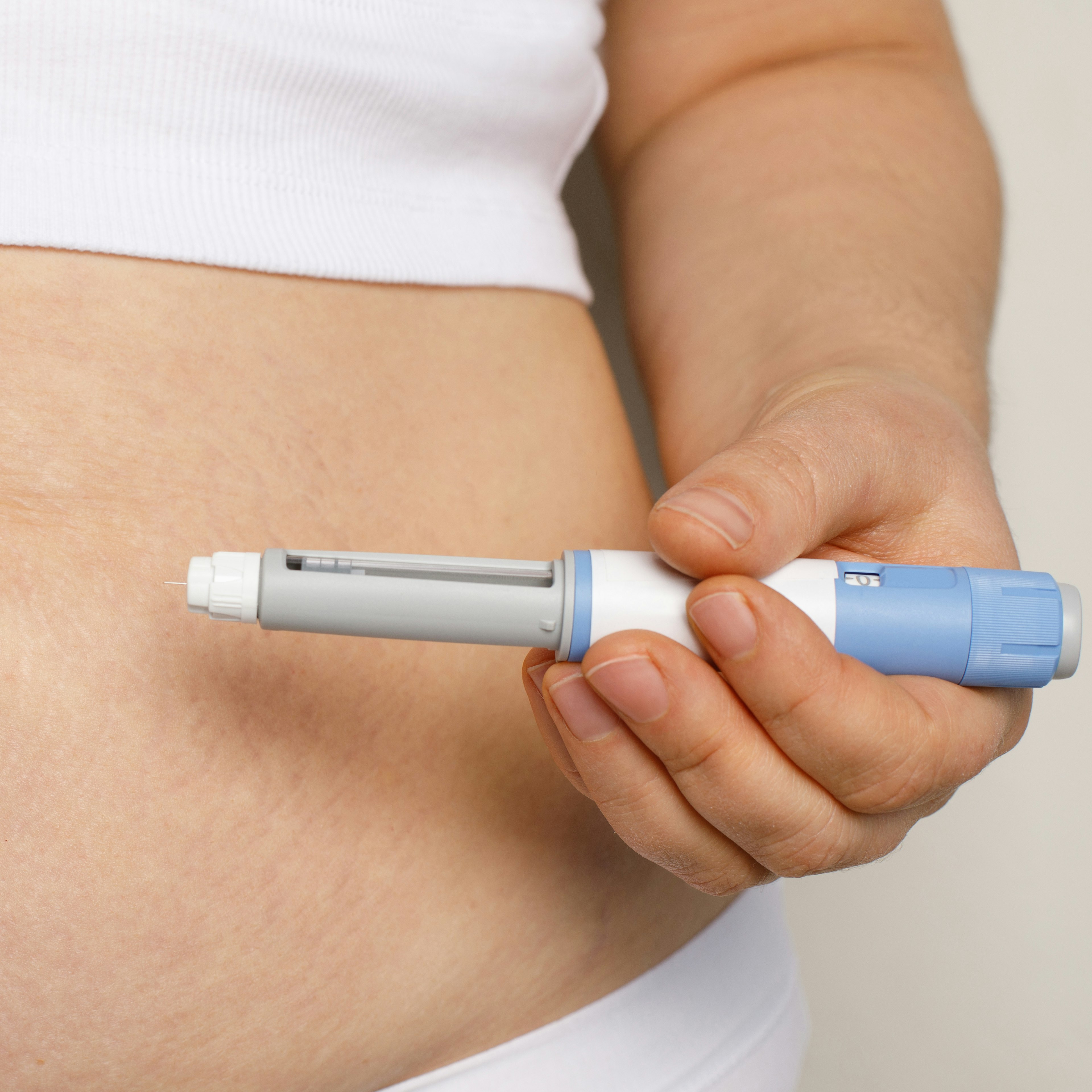 A close-up of a person's stomach with a weight loss injection pressed against it.