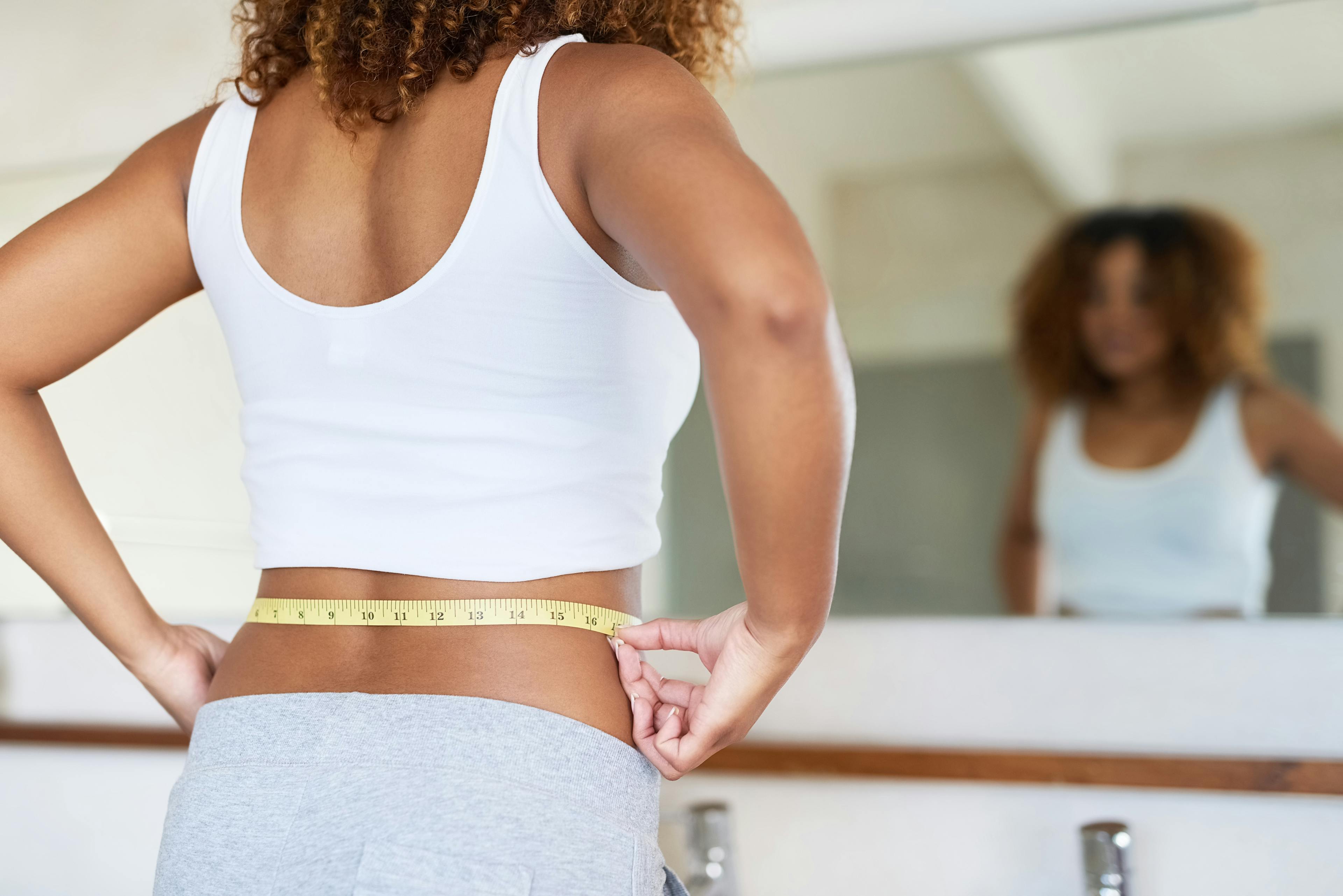 A woman measuring her waist with a tape.