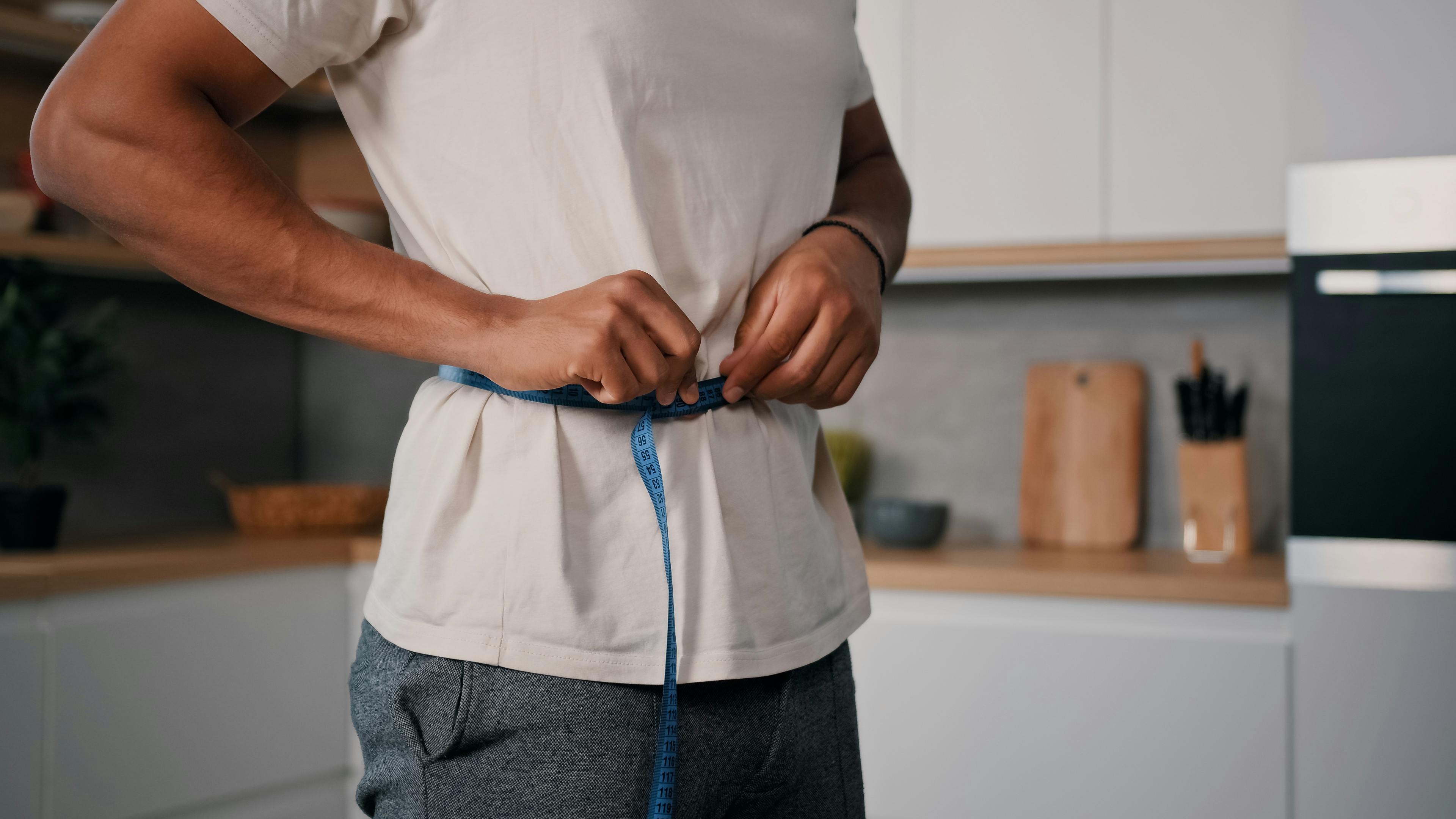A man measures his waist with a tape.
