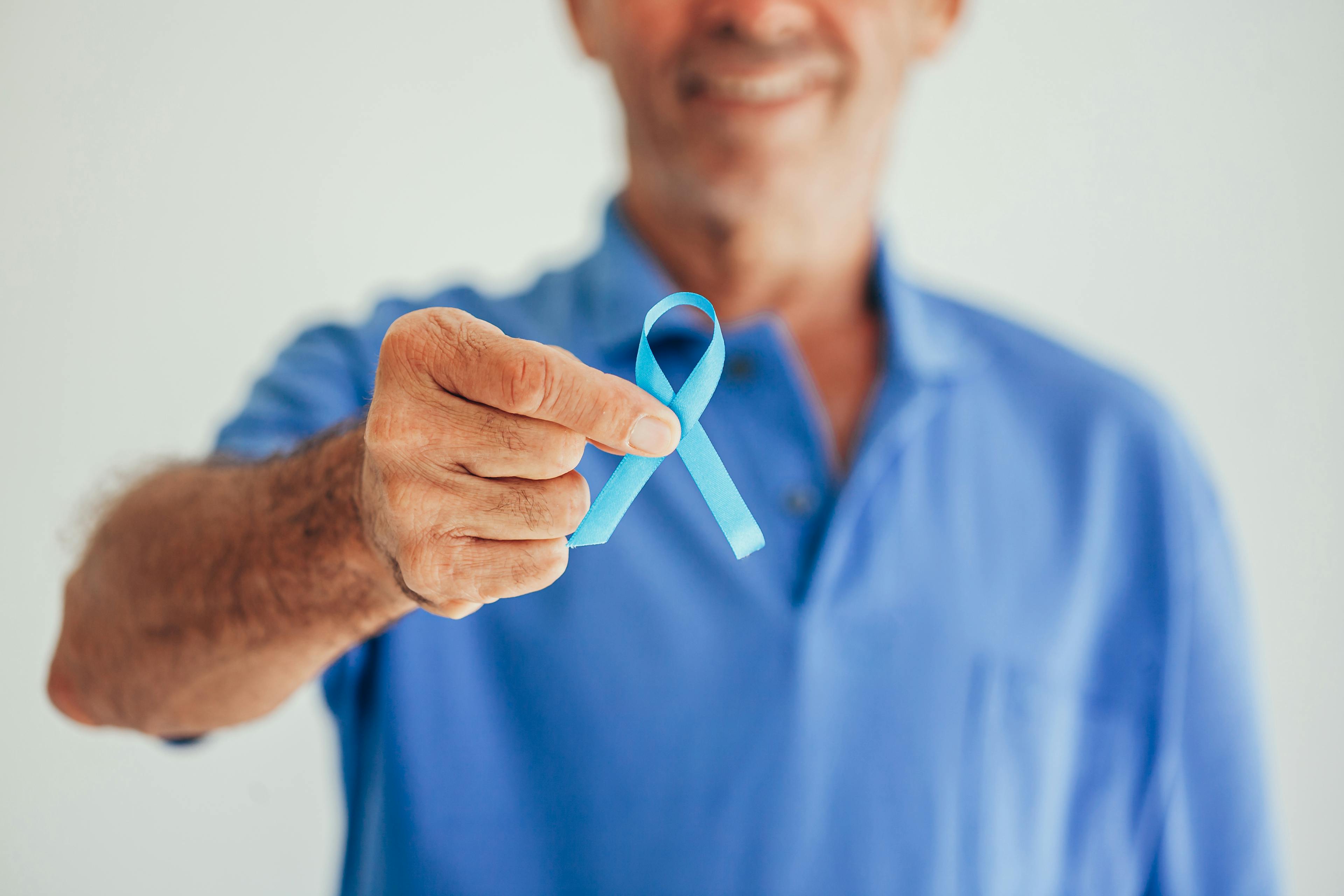 Male cancer survivor holds up blue ribbon.