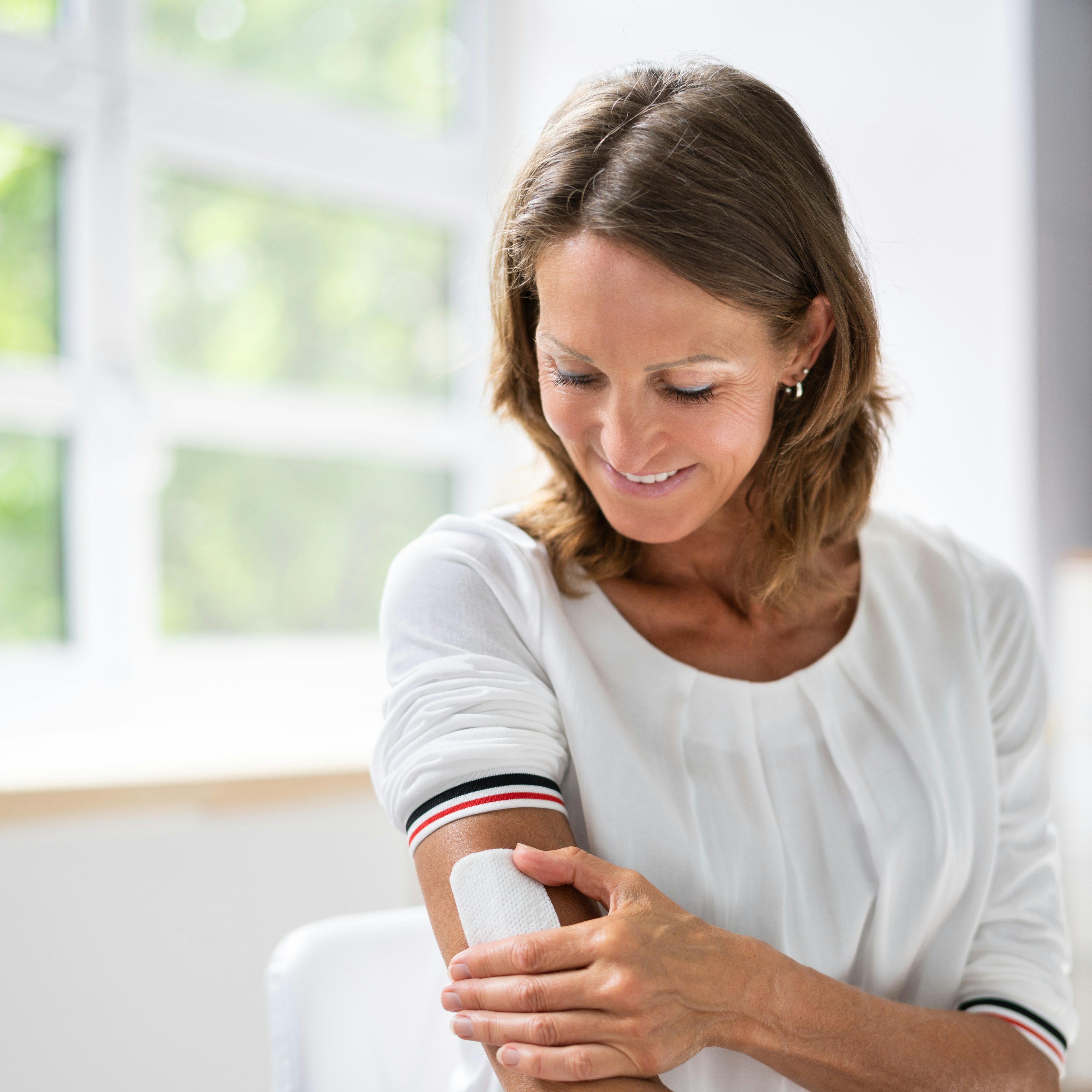 A woman of menopause age is applying a hormone replacement therapy patch. 