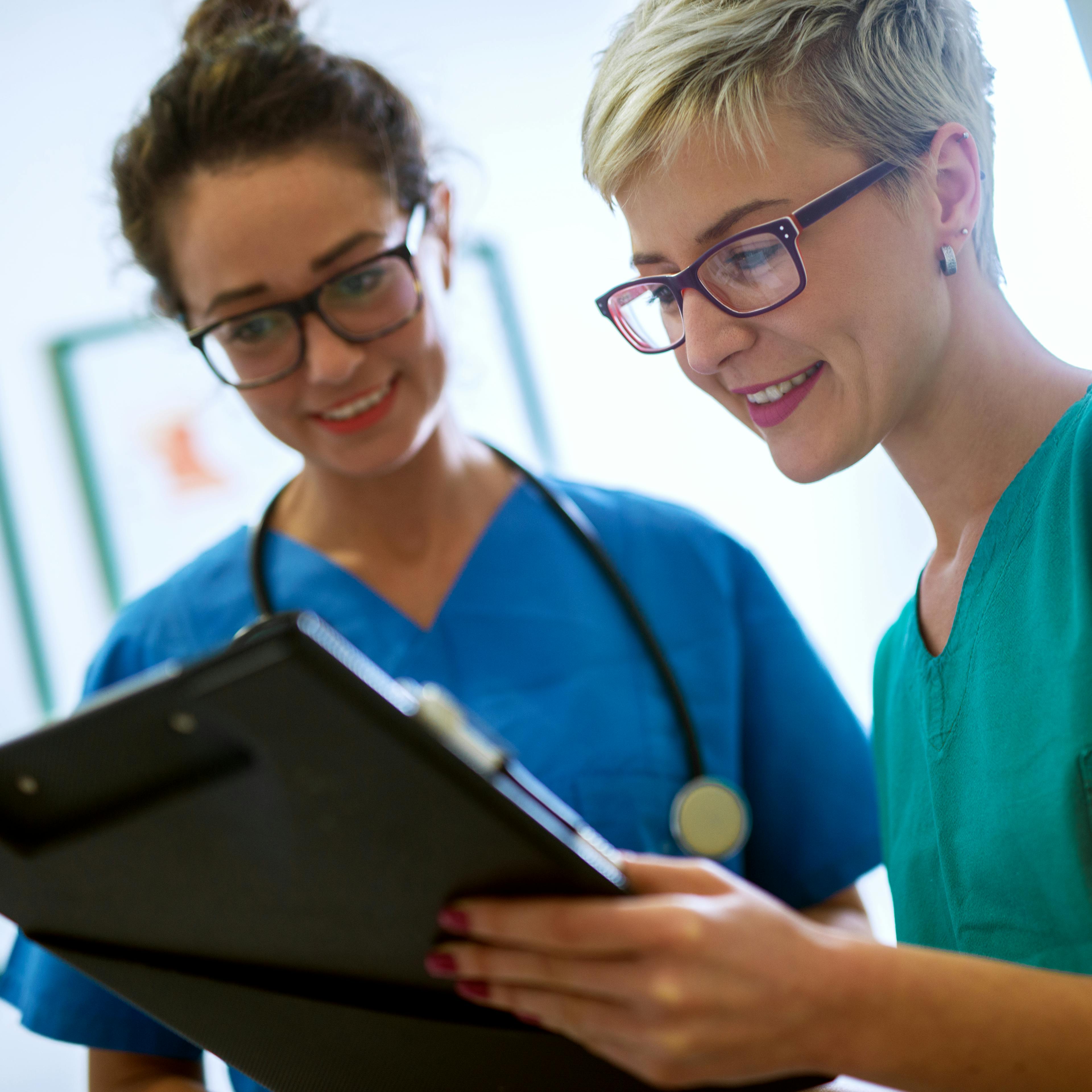 Two female nurses are looking at a clipboard together. 