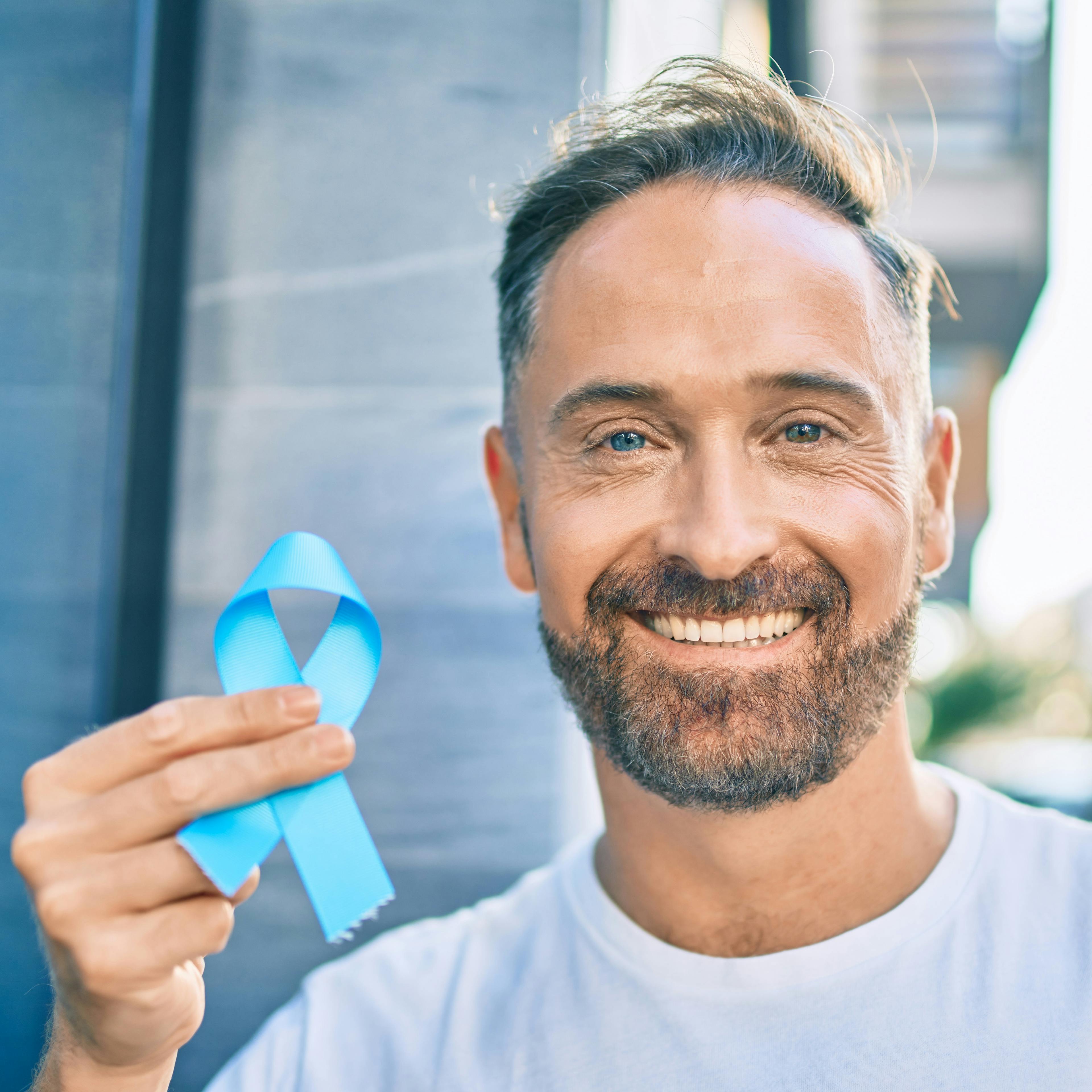 A man is holding up a light blue ribbon, signifying prostate cancer awareness.