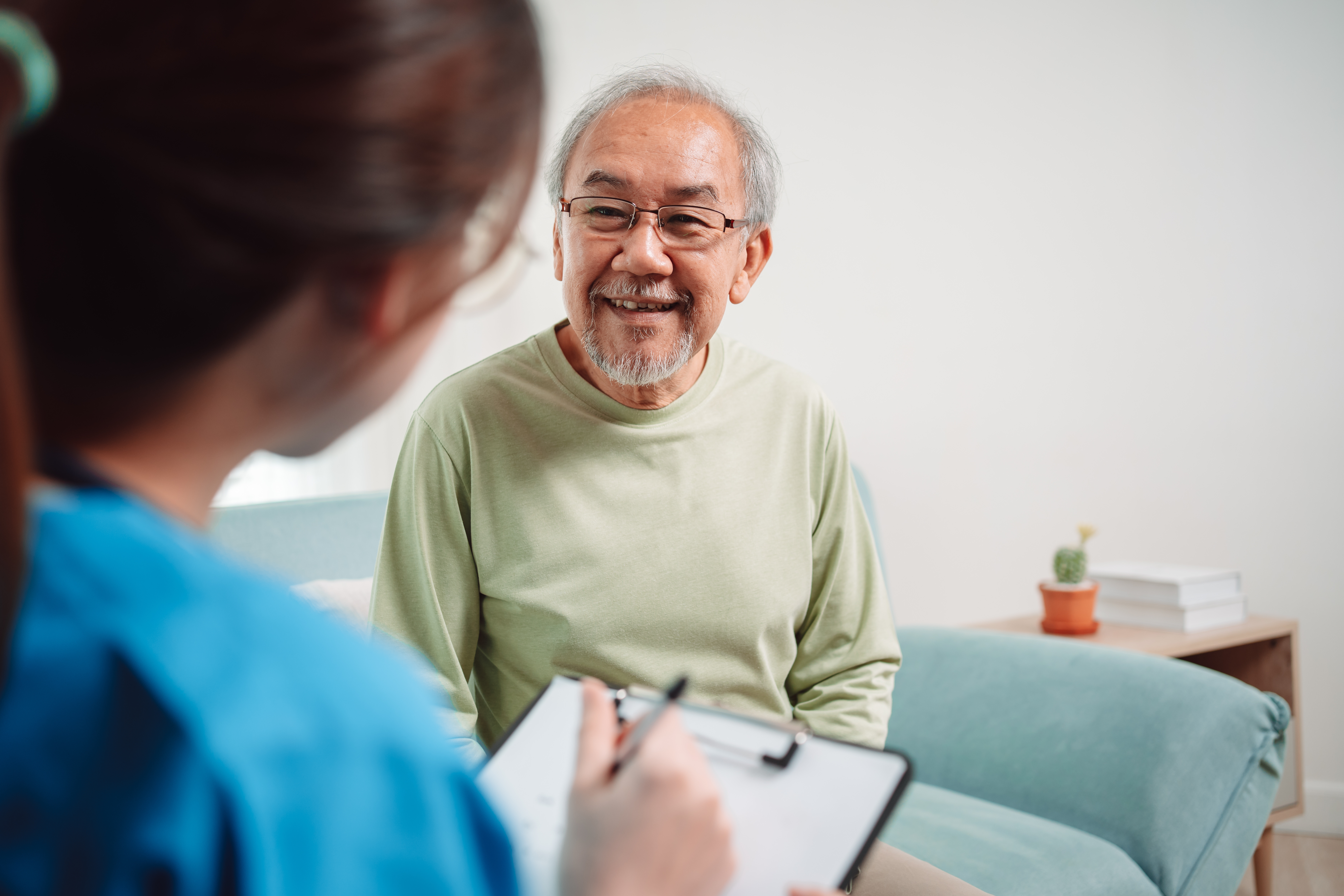 An eldery male patient is speaking to his healthcare provider with a smile on his face.