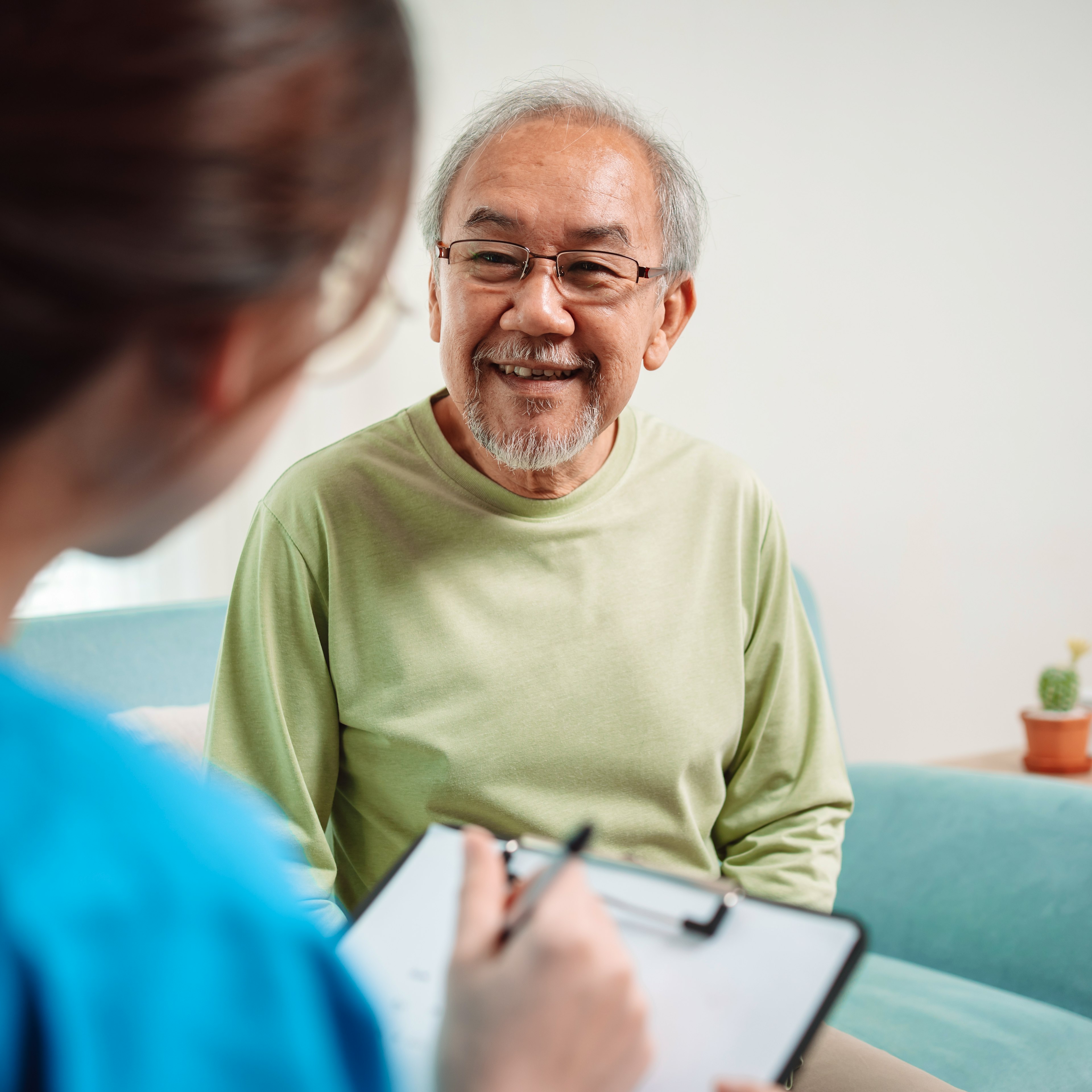 An eldery male patient is speaking to his healthcare provider with a smile on his face.