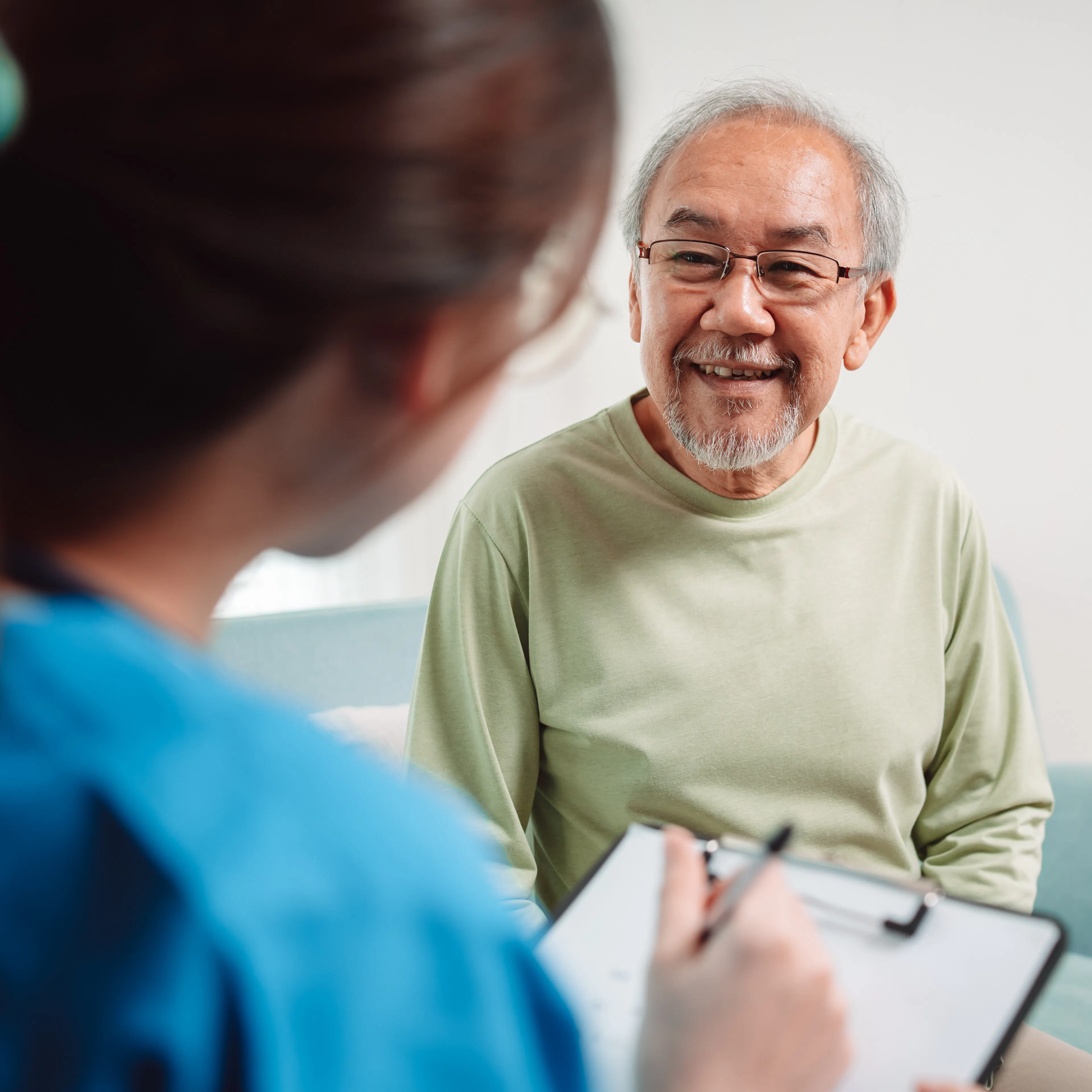An eldery male patient is speaking to his healthcare provider with a smile on his face.