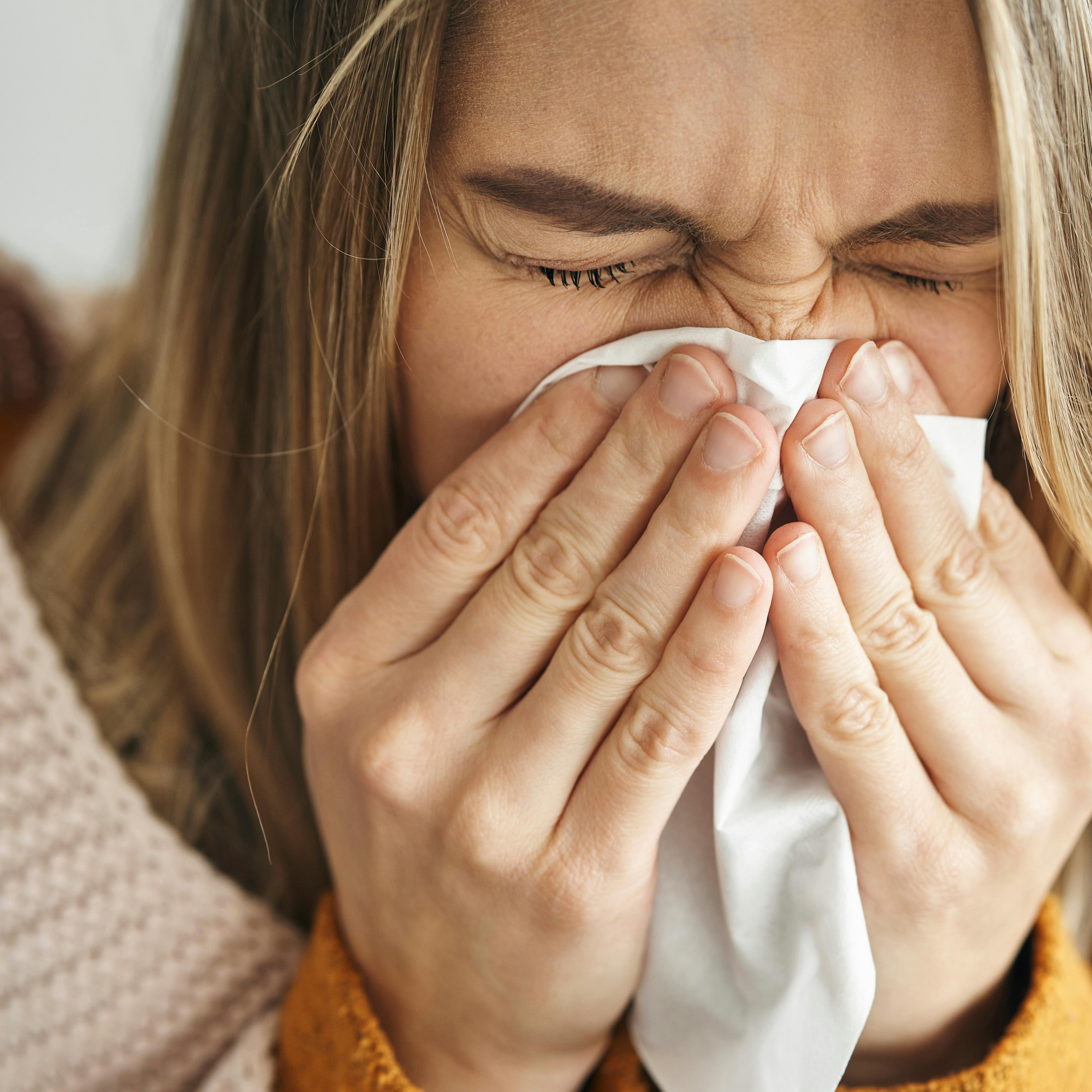 A sick woman is blowing her nose into a tissue. 