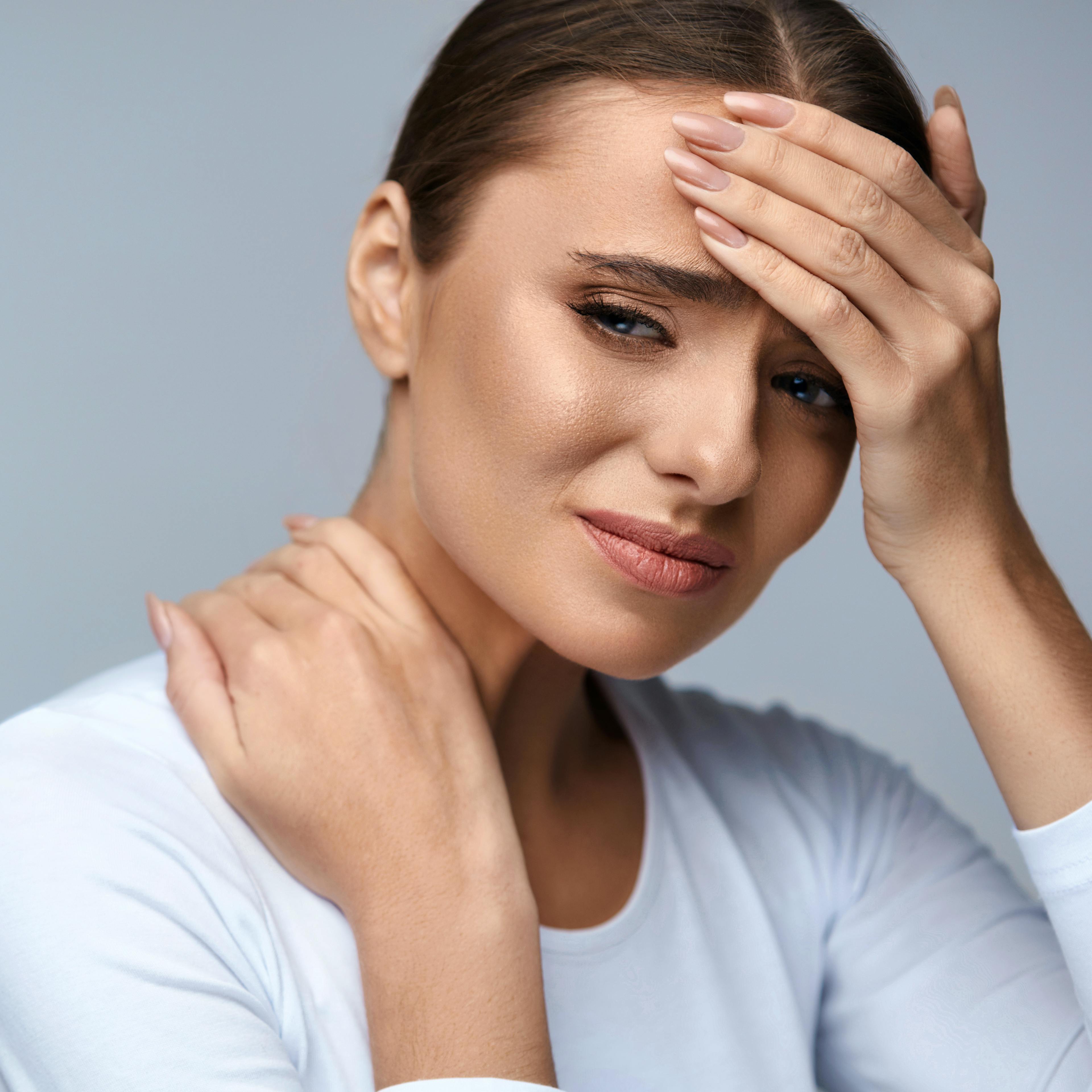 A woman is holding her head and neck in pain.