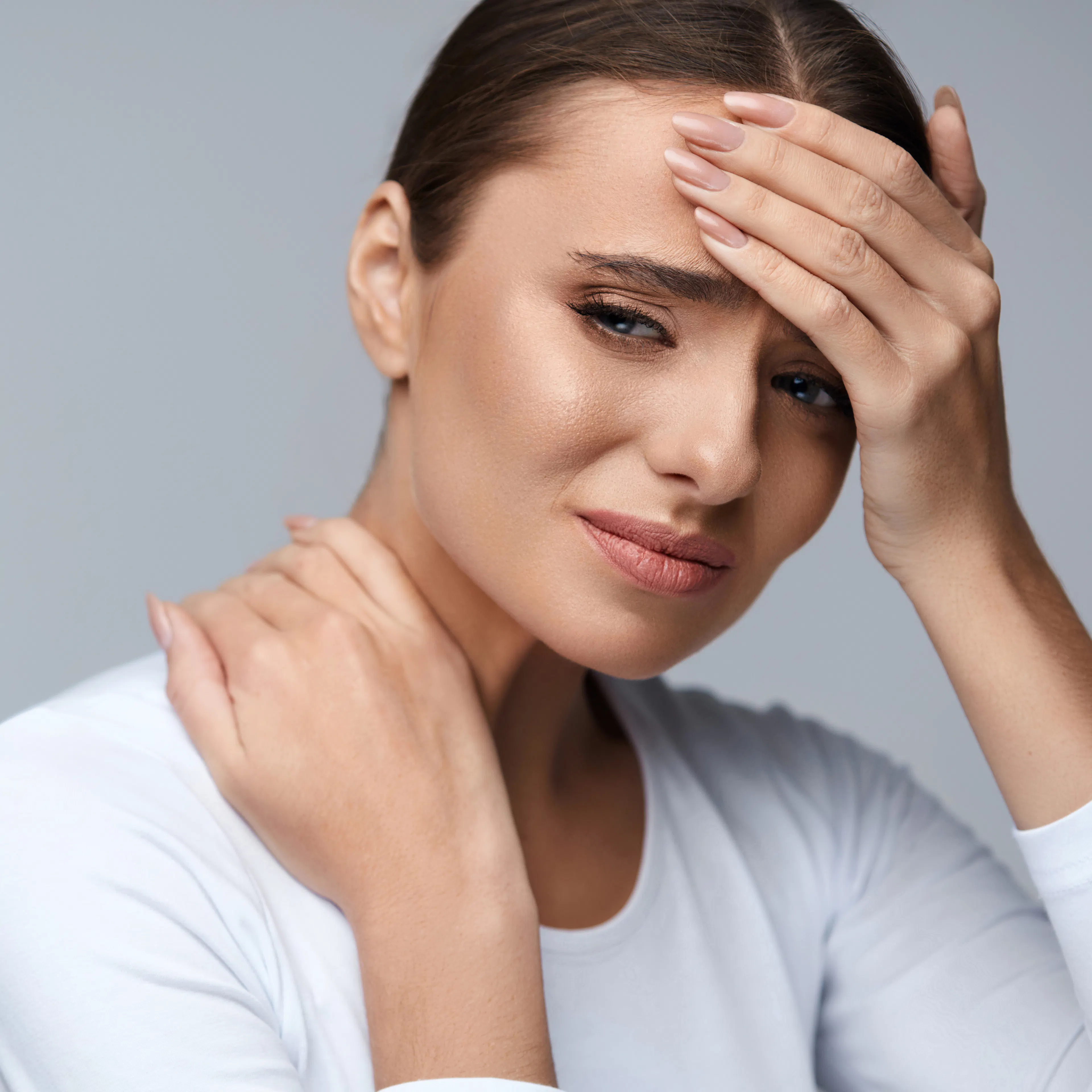A woman is holding her head and neck in pain.