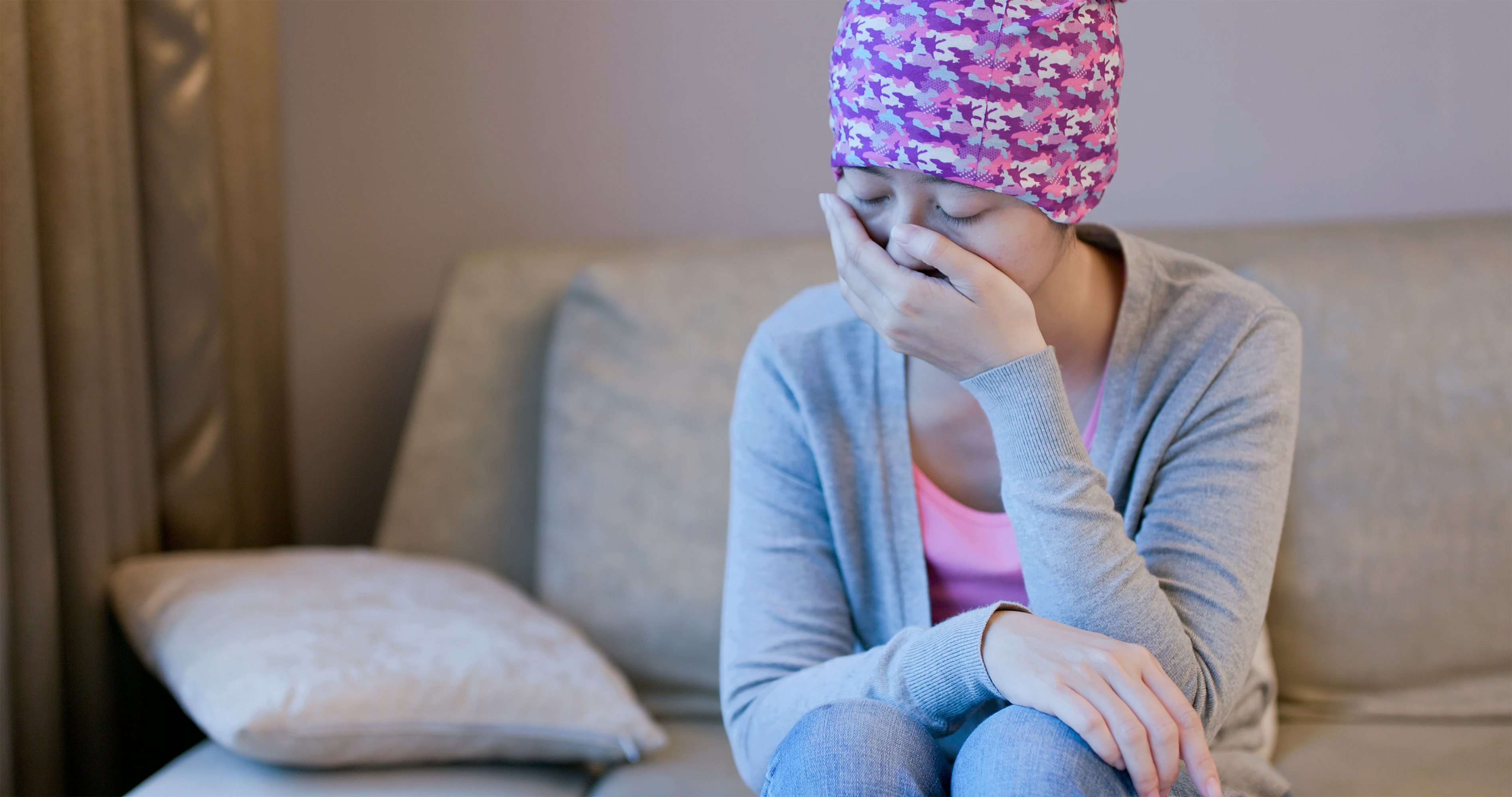 A woman with cancer is sitting on her couch, tired and in pain.